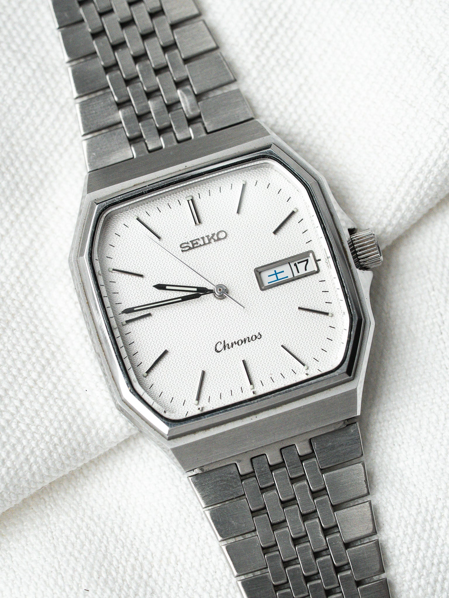 Seiko Chronos vintage watch with white textured dial, date window, and steel bracelet on white fabric