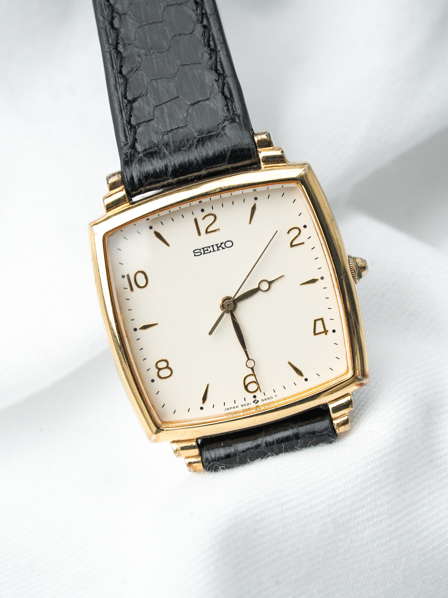 Seiko vintage watch with gold case, white dial, black leather strap on white background