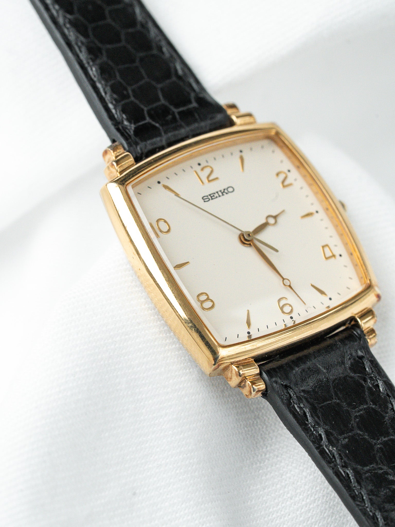 Seiko vintage watch with gold case, white dial, black alligator strap on white background