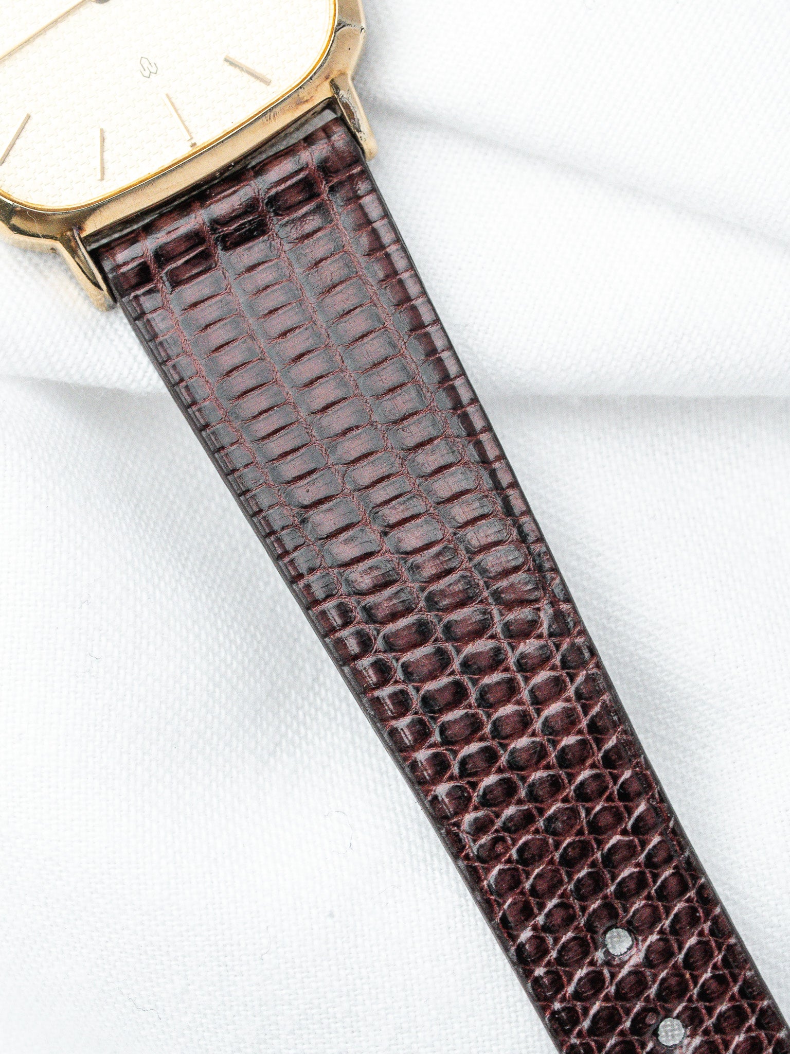 Vintage Cartier watch with gold case, white dial, and brown alligator strap on white fabric