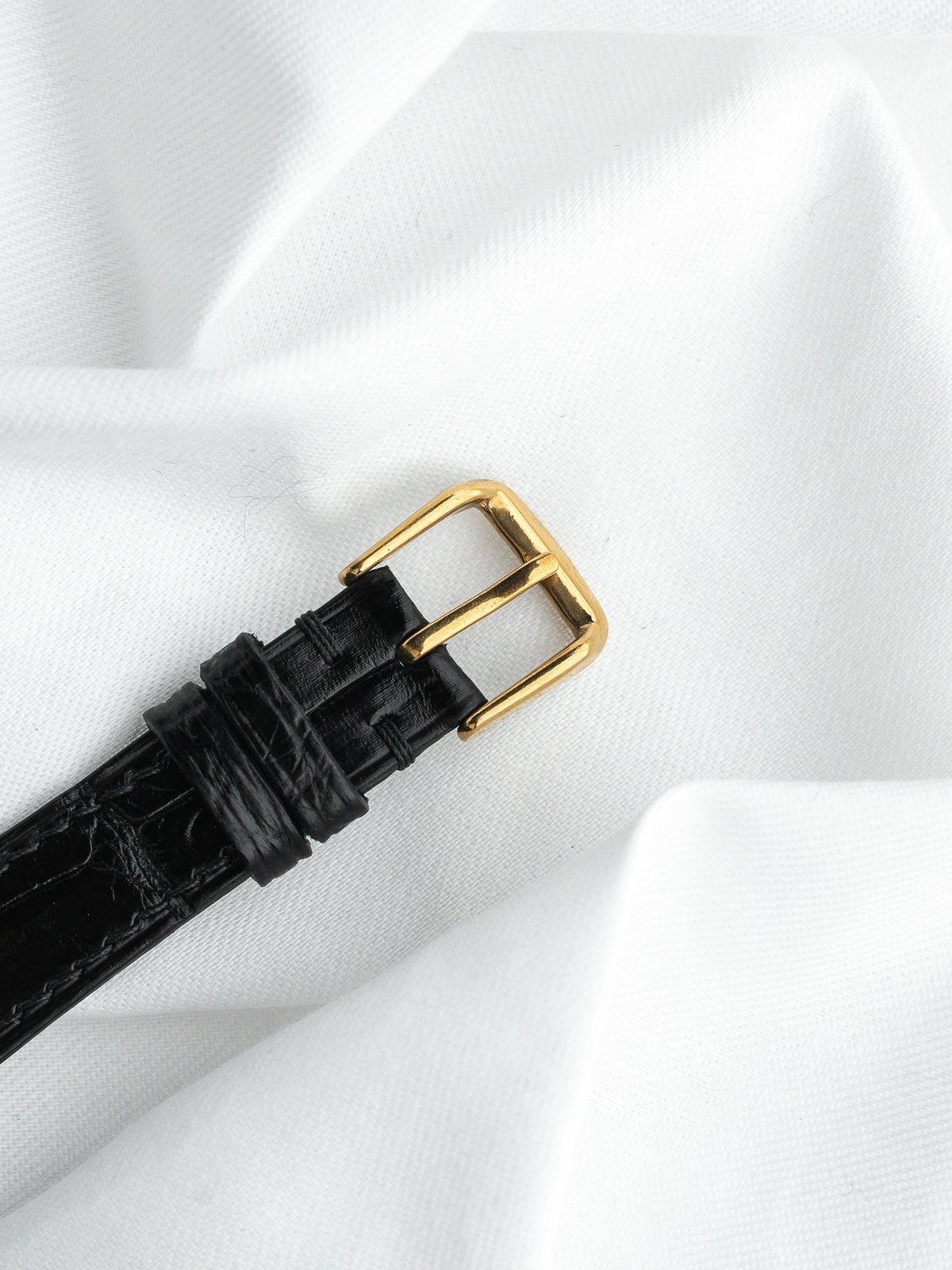 Boucle dorée d'un bracelet de montre en cuir noir grainé sur fond blanc