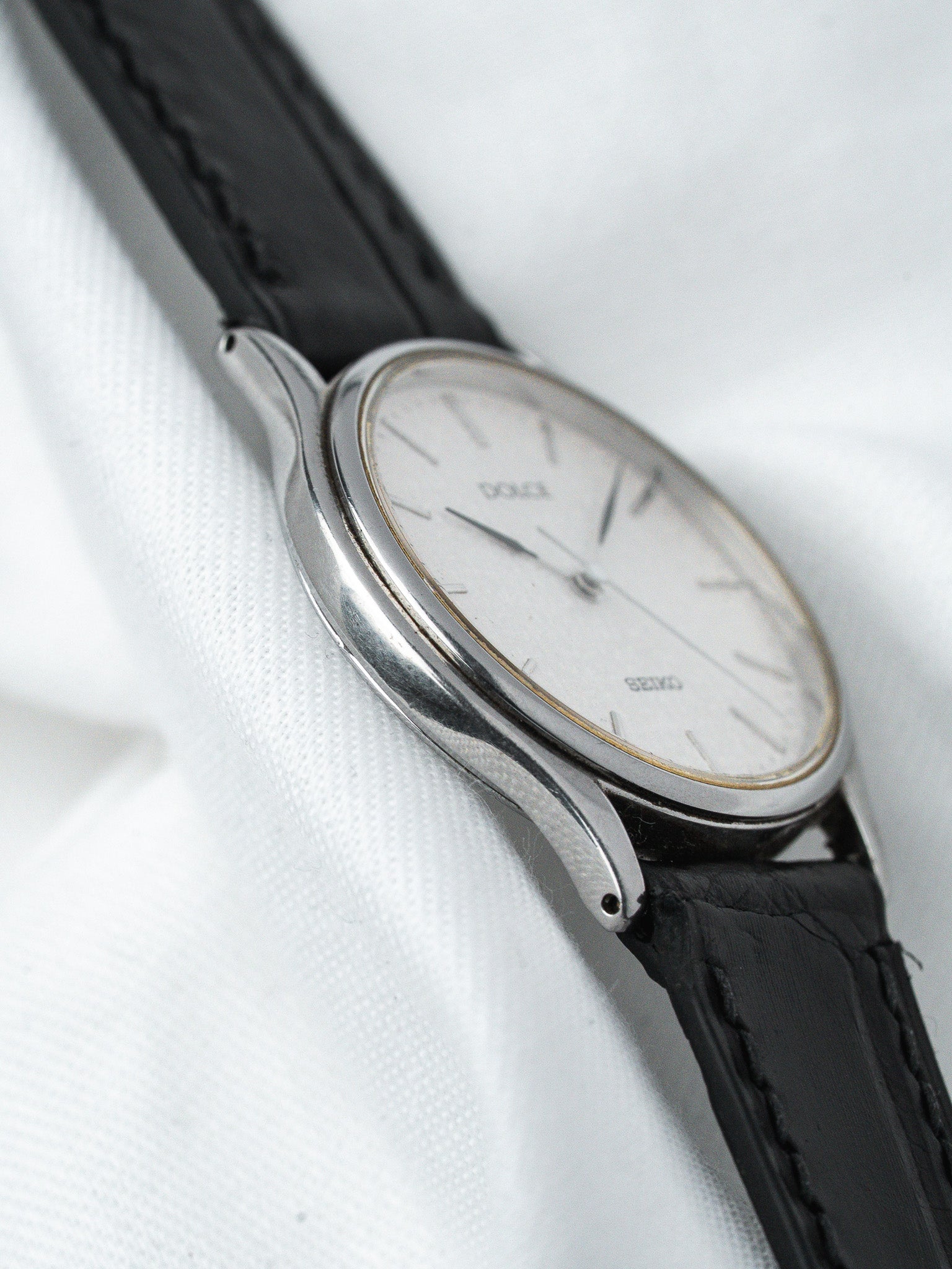 Seiko vintage watch with silver case, white dial, black leather strap on white fabric