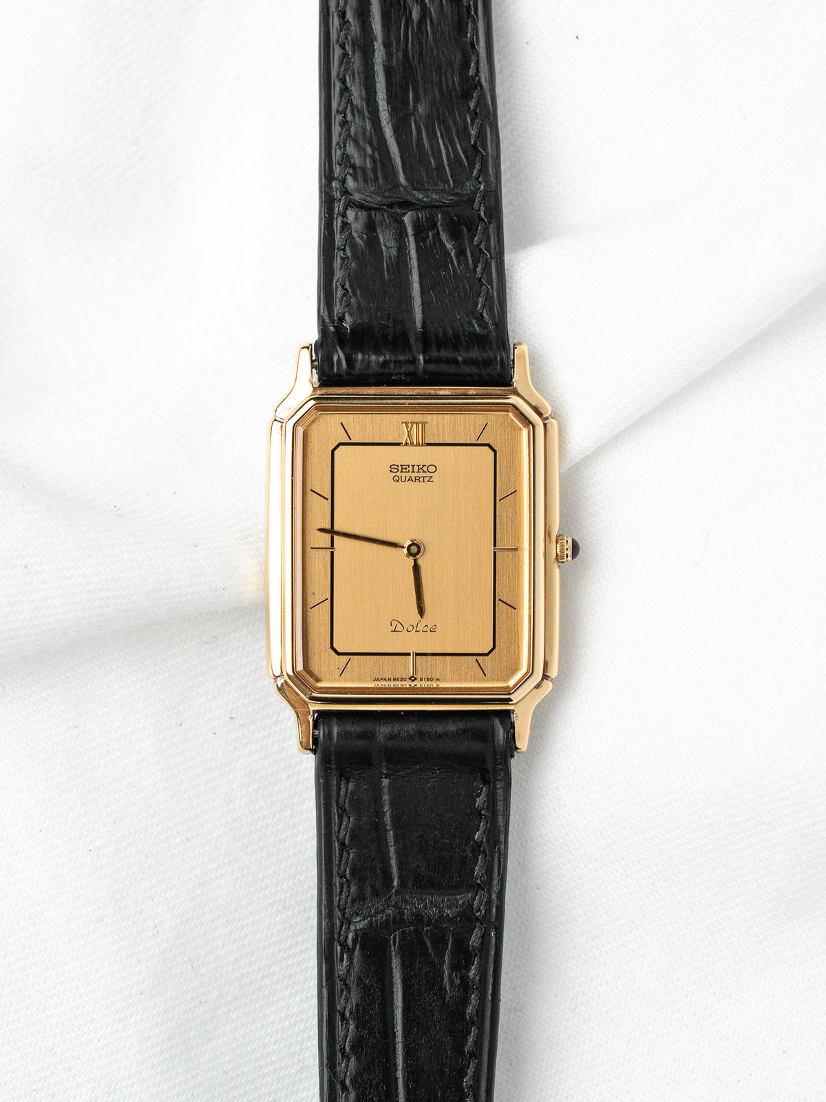 Seiko Dolce vintage watch with gold case, black leather strap, and gold dial on white background