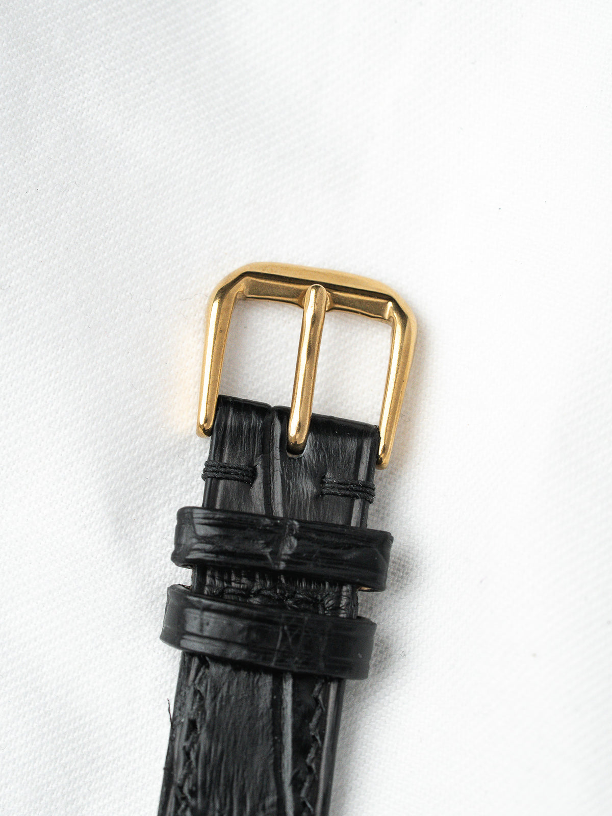 Black textured leather watch strap with gold buckle on white background