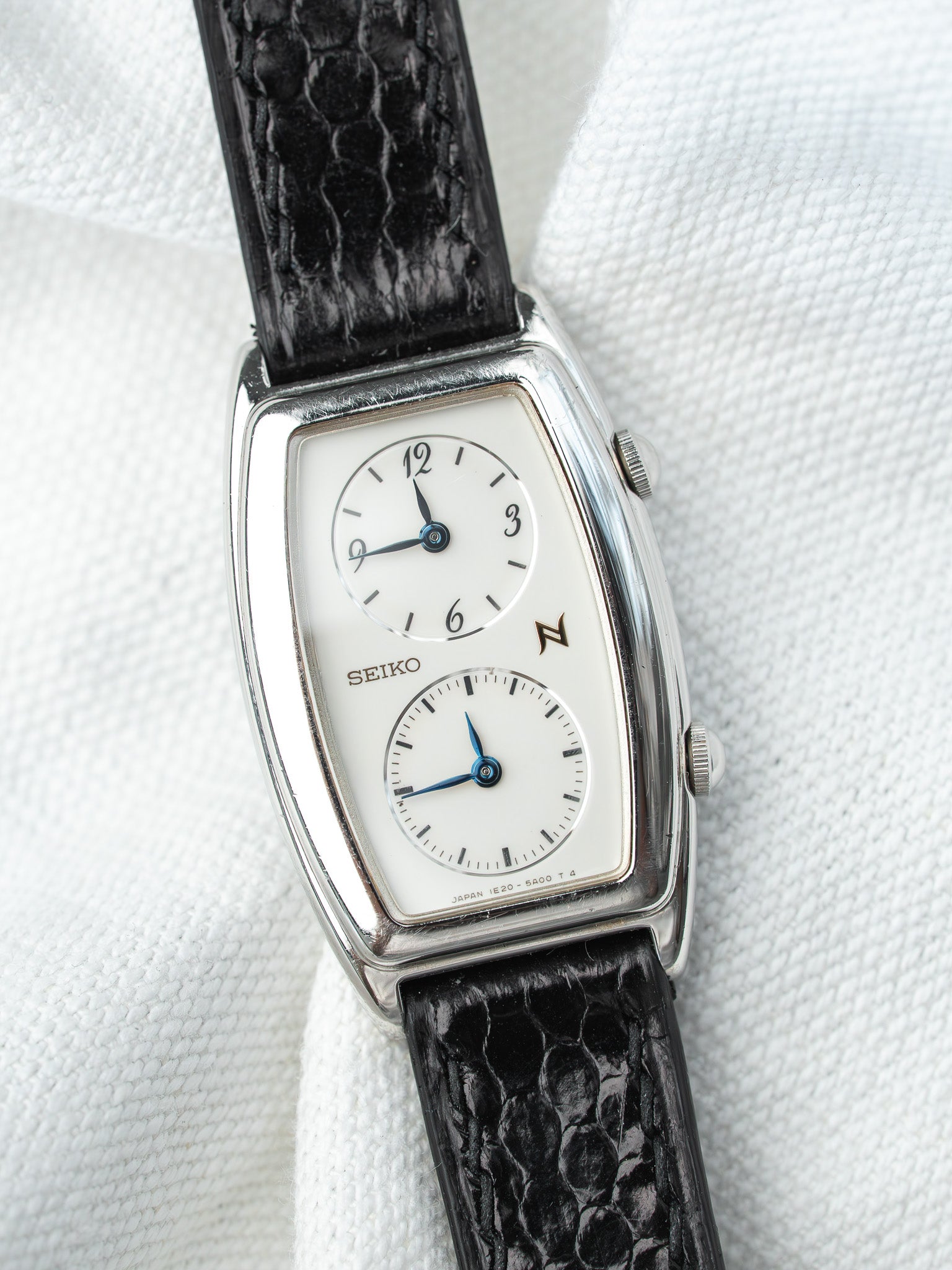 Seiko vintage watch with white dial, black lizard strap, silver case on white fabric