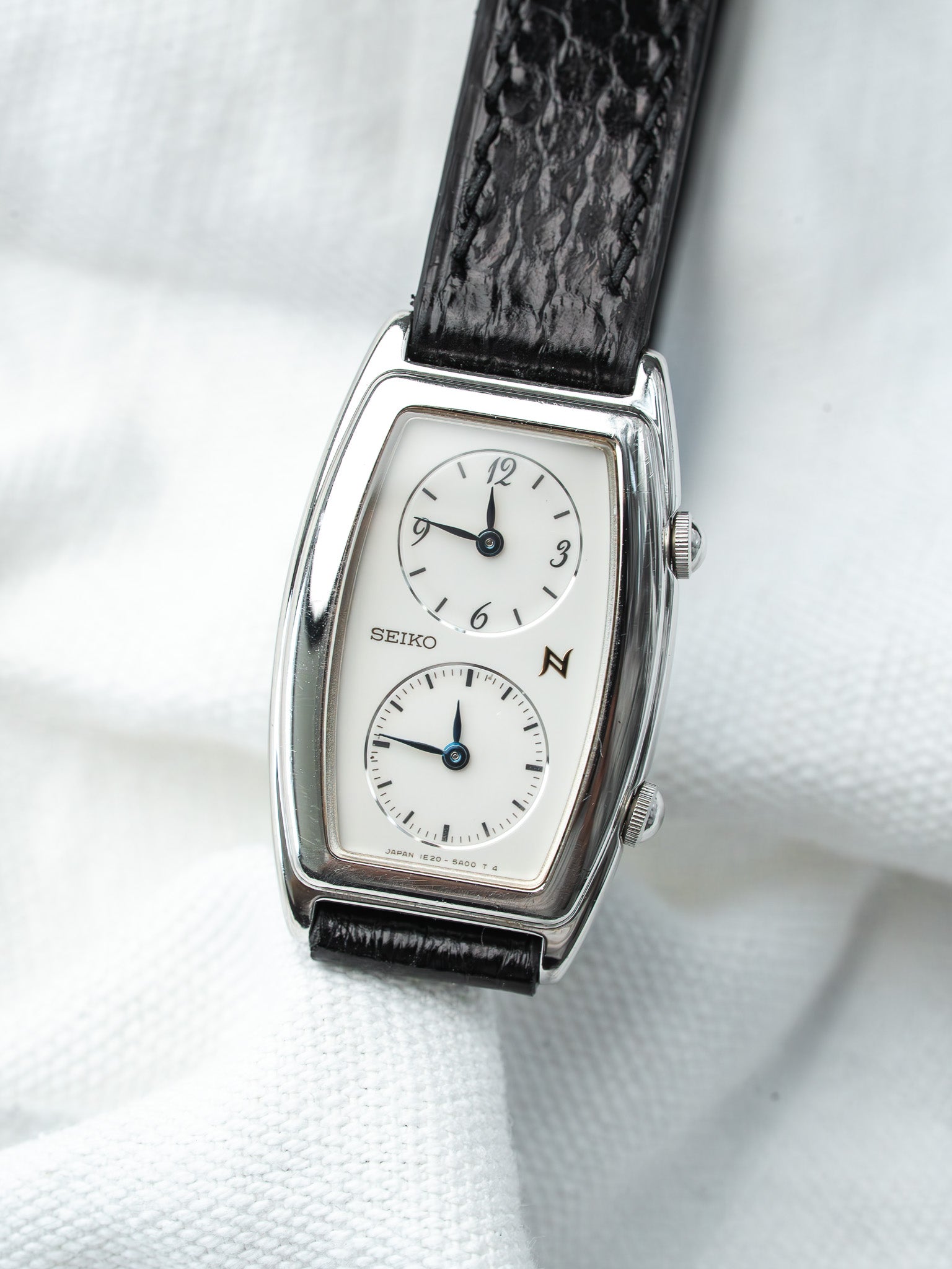 Seiko vintage watch with white dial, black leather strap, rectangular case on white fabric