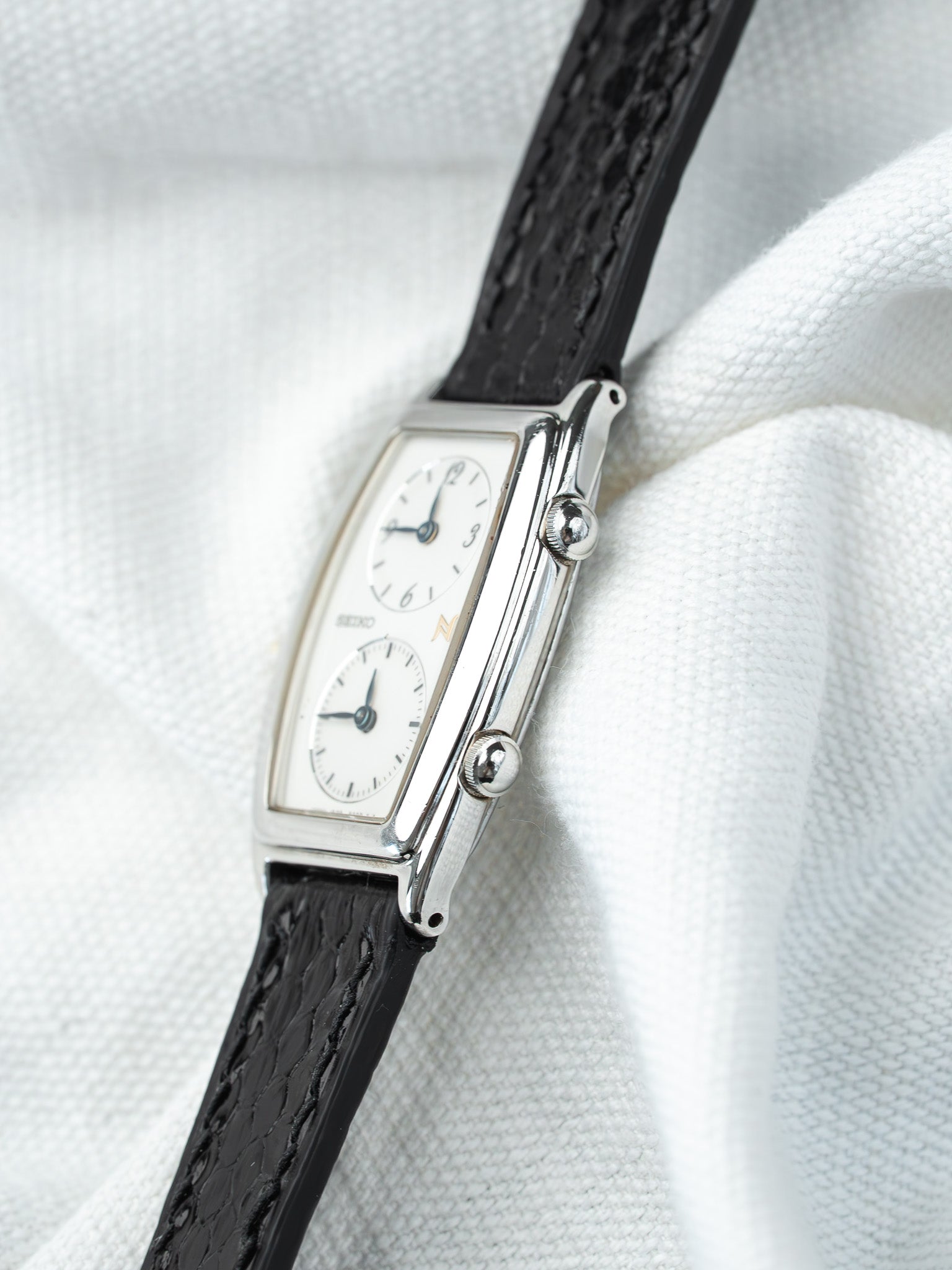 Seiko vintage watch with white dial, black leather strap, rectangular case on white fabric