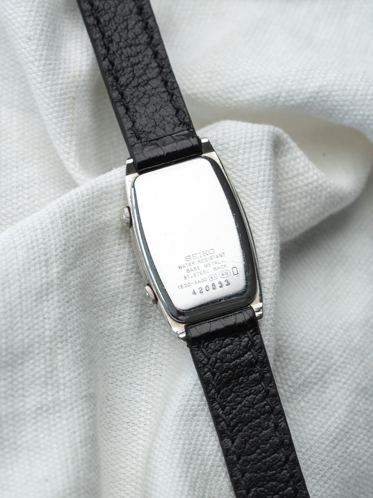 Seiko vintage watch with black leather strap, stainless steel back, resting on white fabric