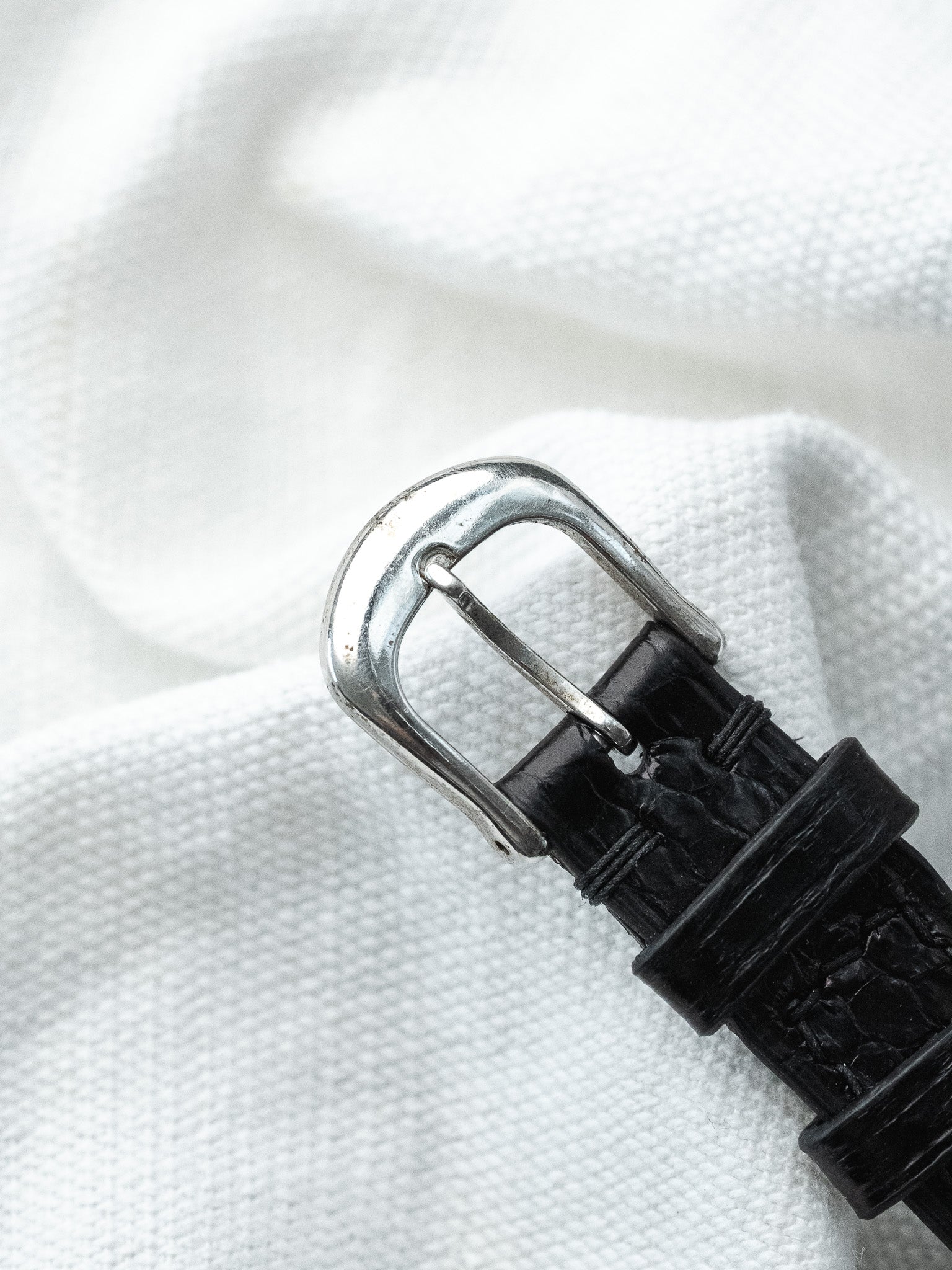 Vintage watch strap with black alligator leather and silver buckle on white fabric