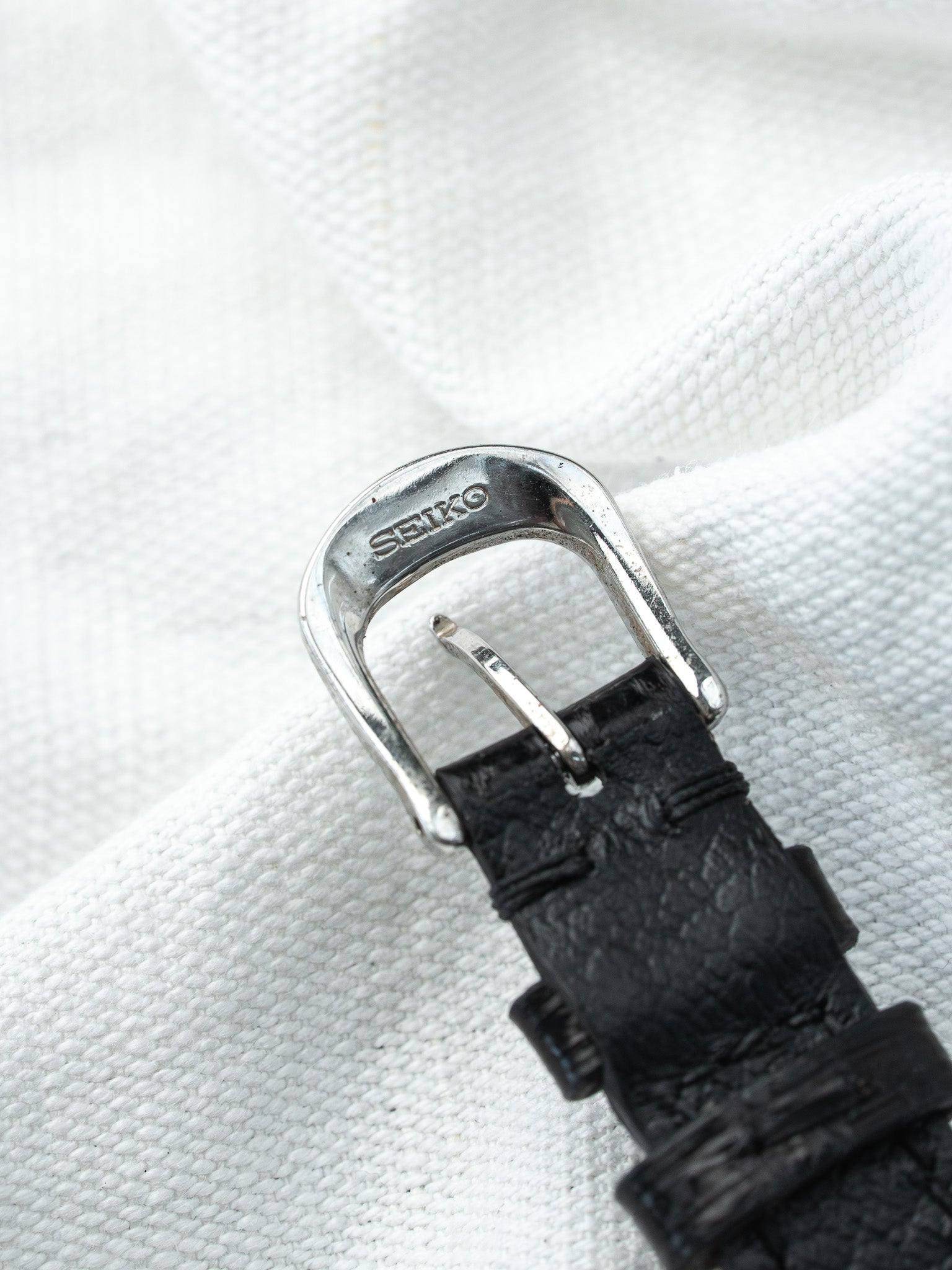 Seiko watch buckle with black textured strap on white fabric background