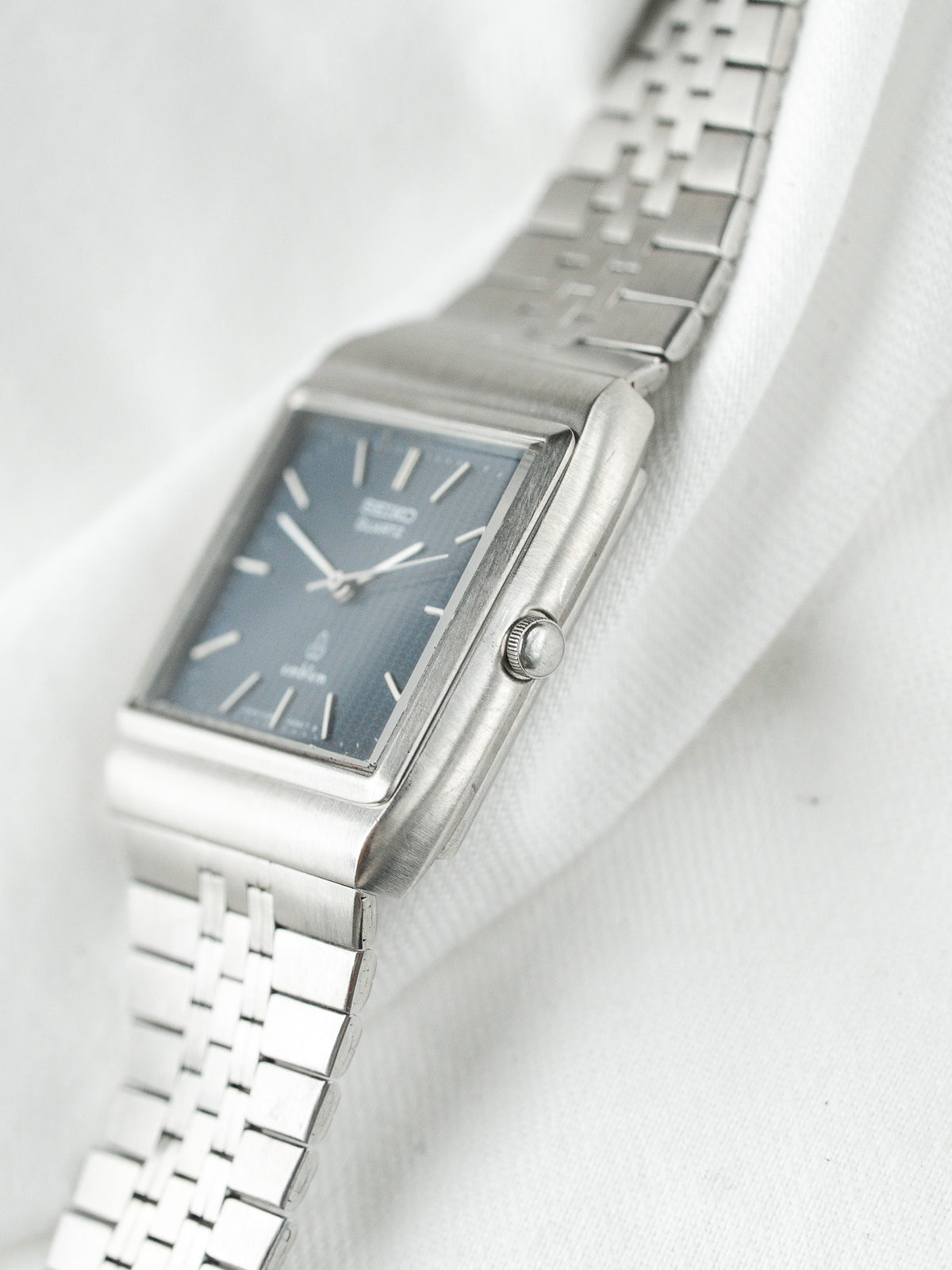 Montre Seiko vintage en acier, boîtier rectangulaire et cadran bleu sur fond blanc