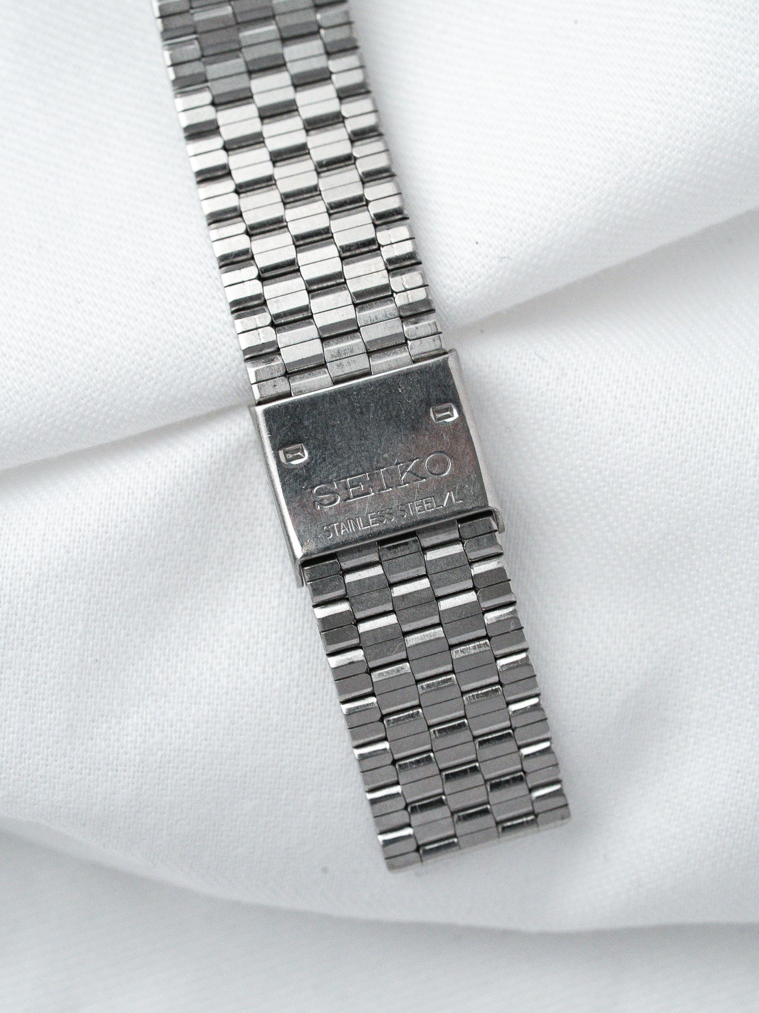 Seiko stainless steel watch bracelet with engraved clasp on white fabric