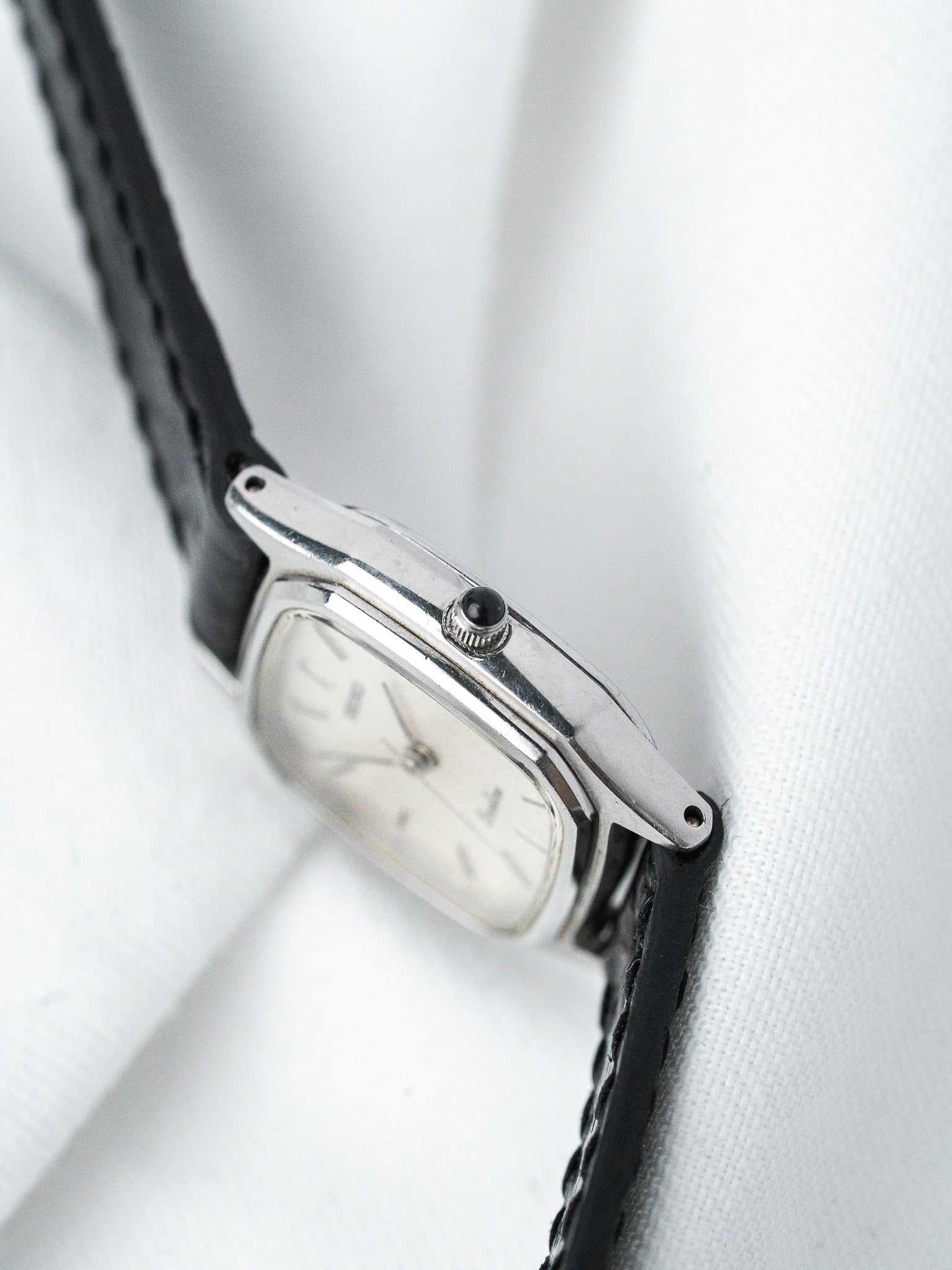 Vintage Cartier watch with silver case, white dial, black leather strap on white fabric