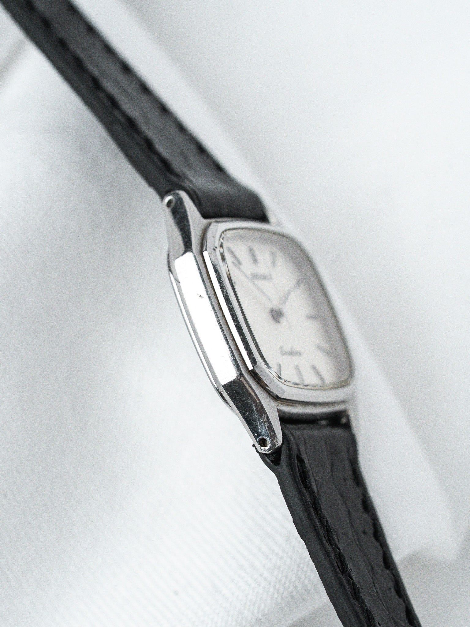 Vintage Seiko watch with silver case, white dial, black leather strap on white fabric