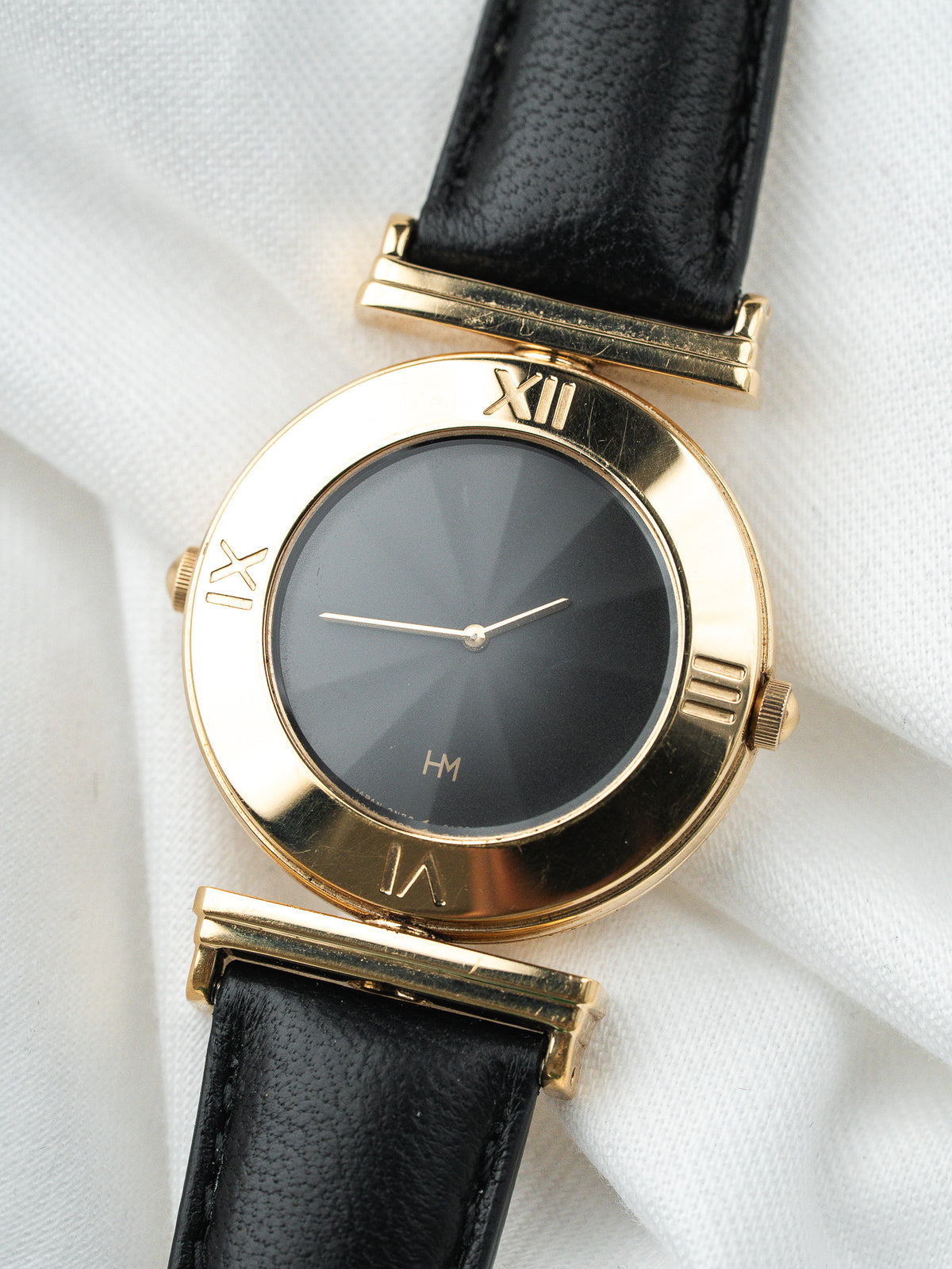 Montre HM vintage, boîtier rond doré, cadran noir et bracelet en cuir noir