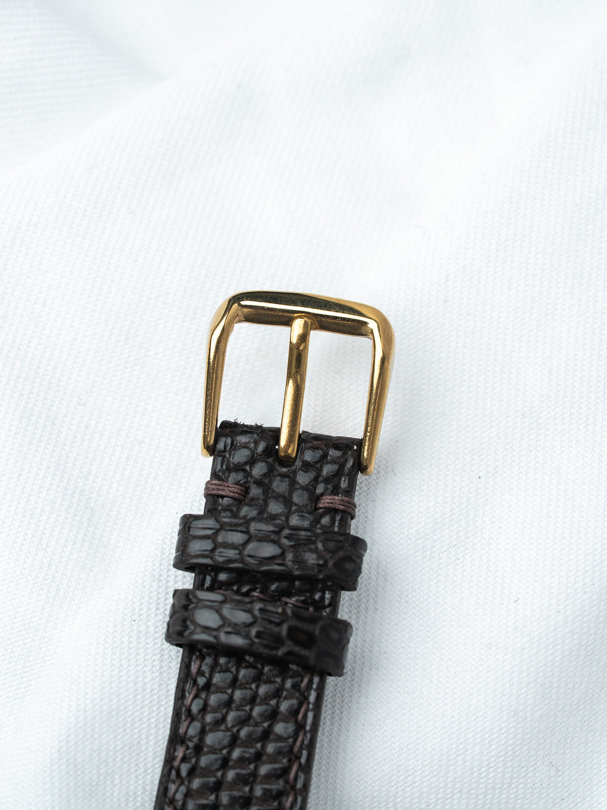 Brown alligator leather watch strap with gold buckle on white background