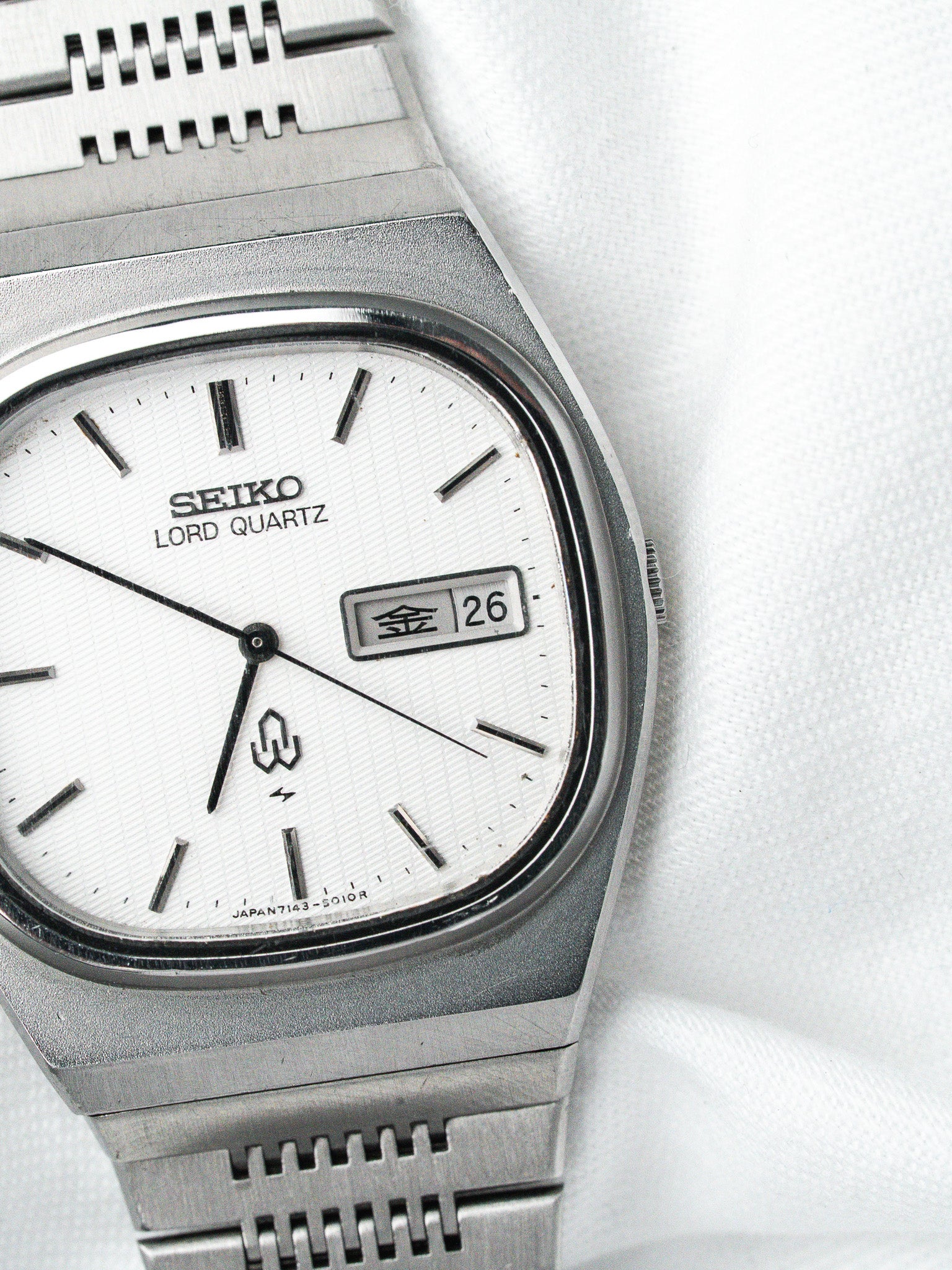 Seiko Lord Quartz vintage watch with white dial, day-date display, and steel bracelet on white fabric