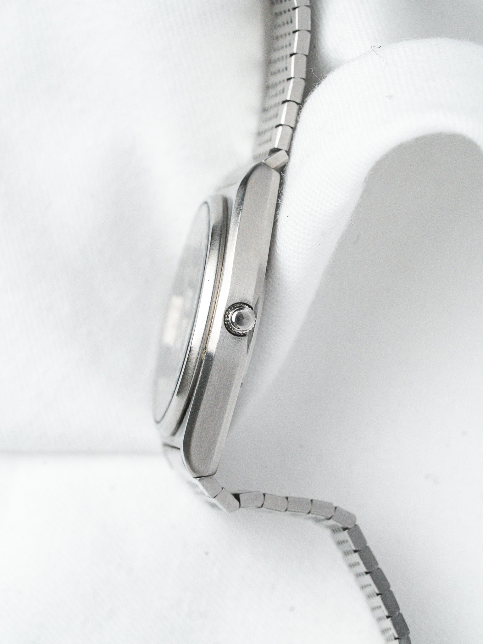 Vintage Omega watch with stainless steel case and bracelet, side profile on white fabric