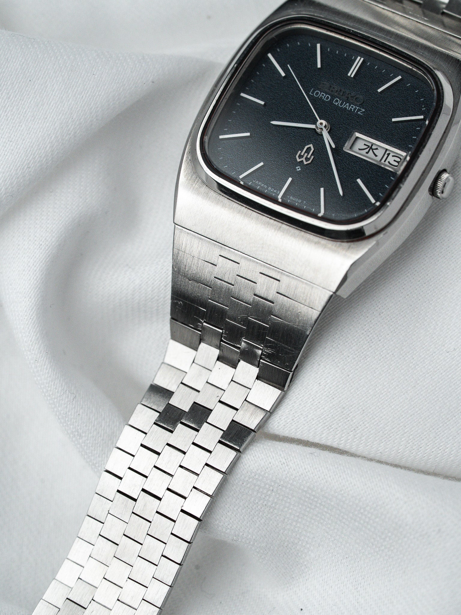 Seiko Lord Quartz vintage watch with black dial, silver case, and woven bracelet on white fabric