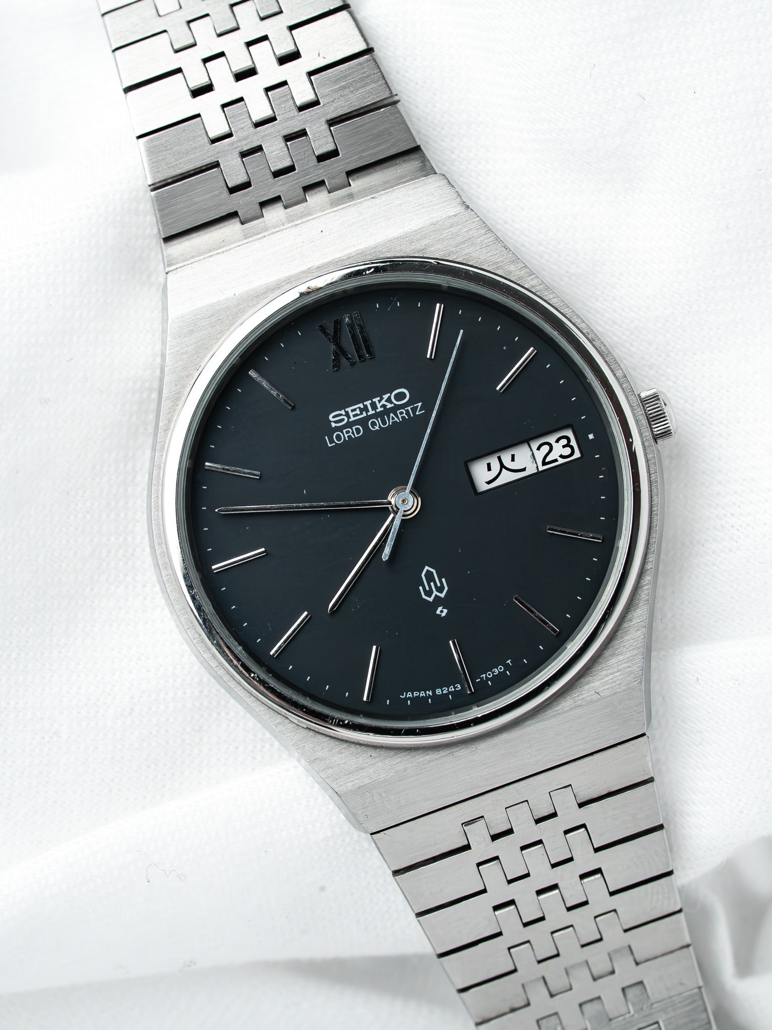Seiko Lord Quartz vintage watch with black dial, steel case, and patterned bracelet on white background