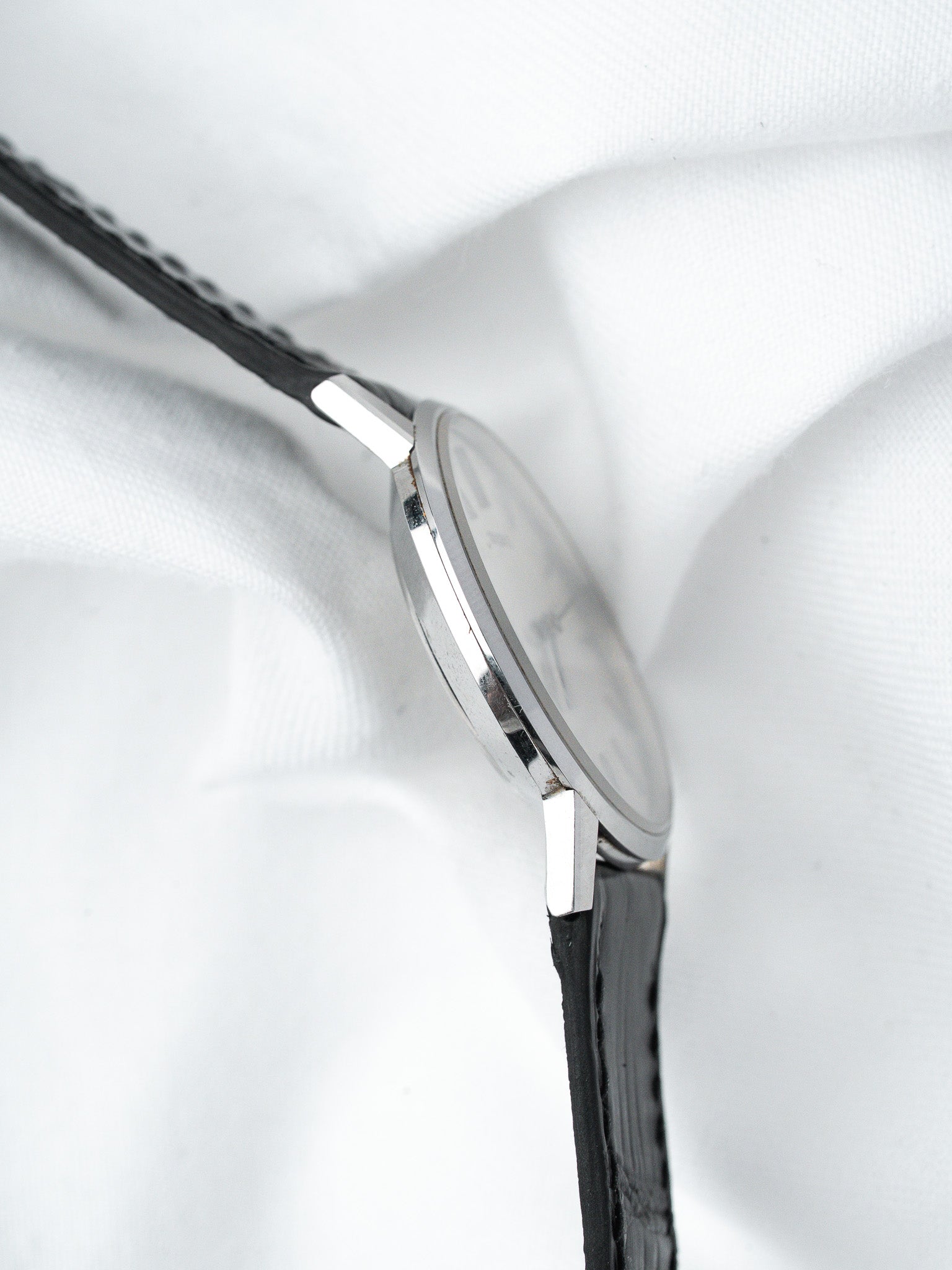 Vintage Omega watch with black leather strap, silver case, white dial on white fabric