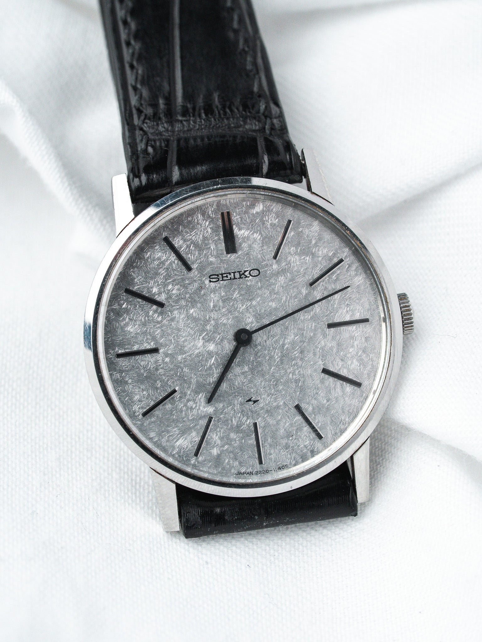 Seiko vintage watch with textured silver dial, black leather strap, on white fabric