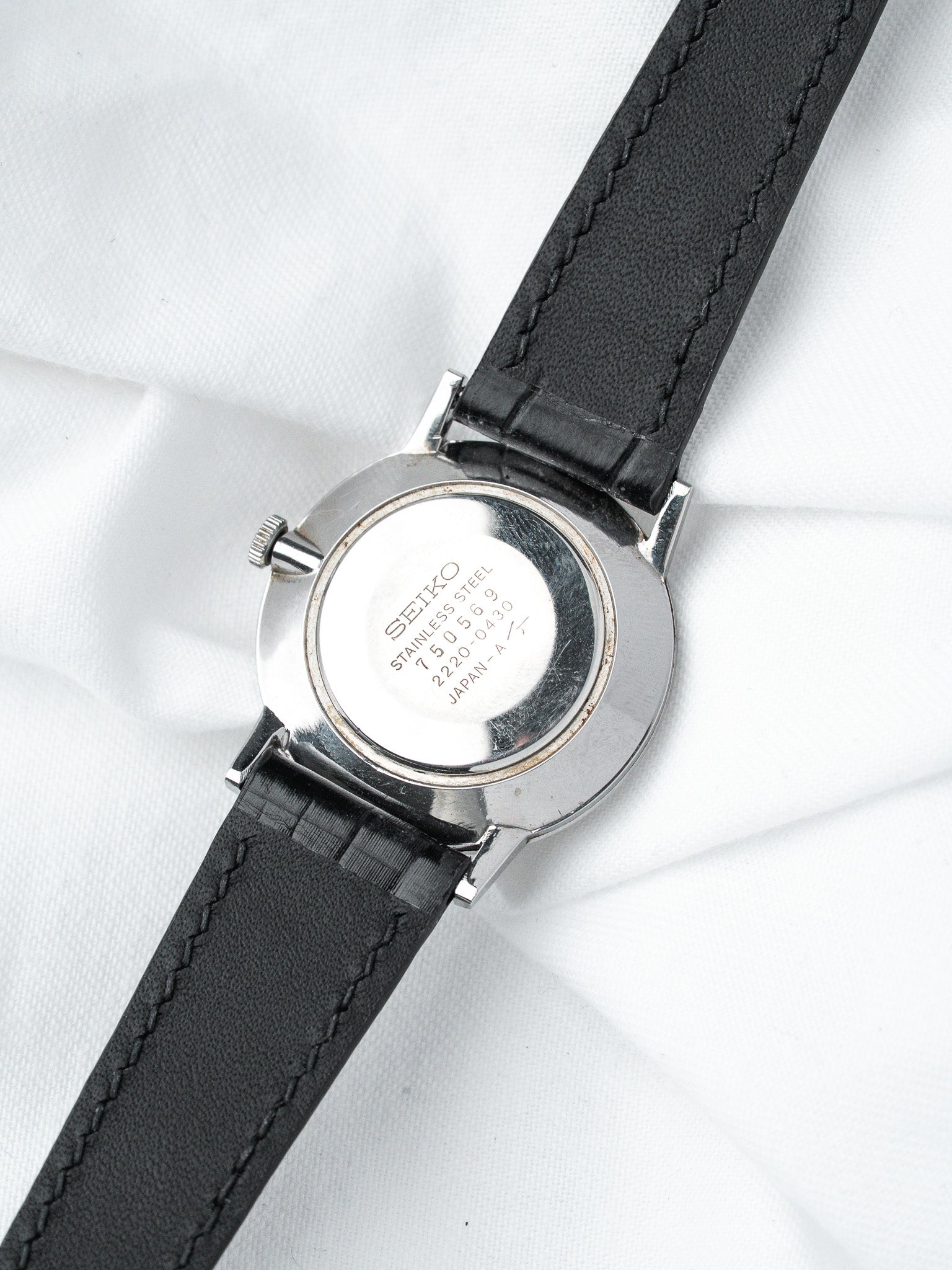 Seiko vintage watch back stainless steel with black leather strap on white fabric