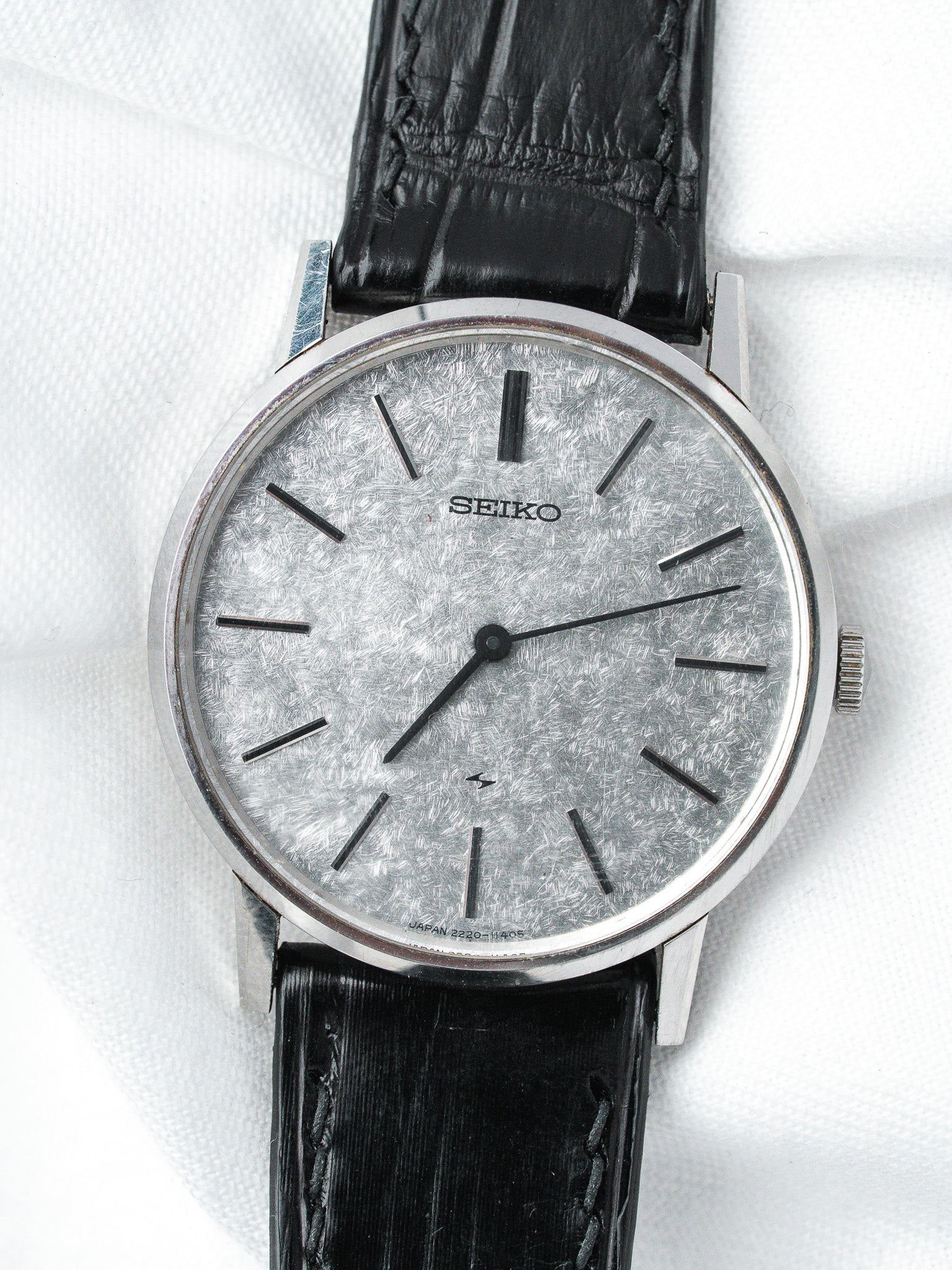 Seiko vintage watch with textured silver dial, black leather strap, and steel case