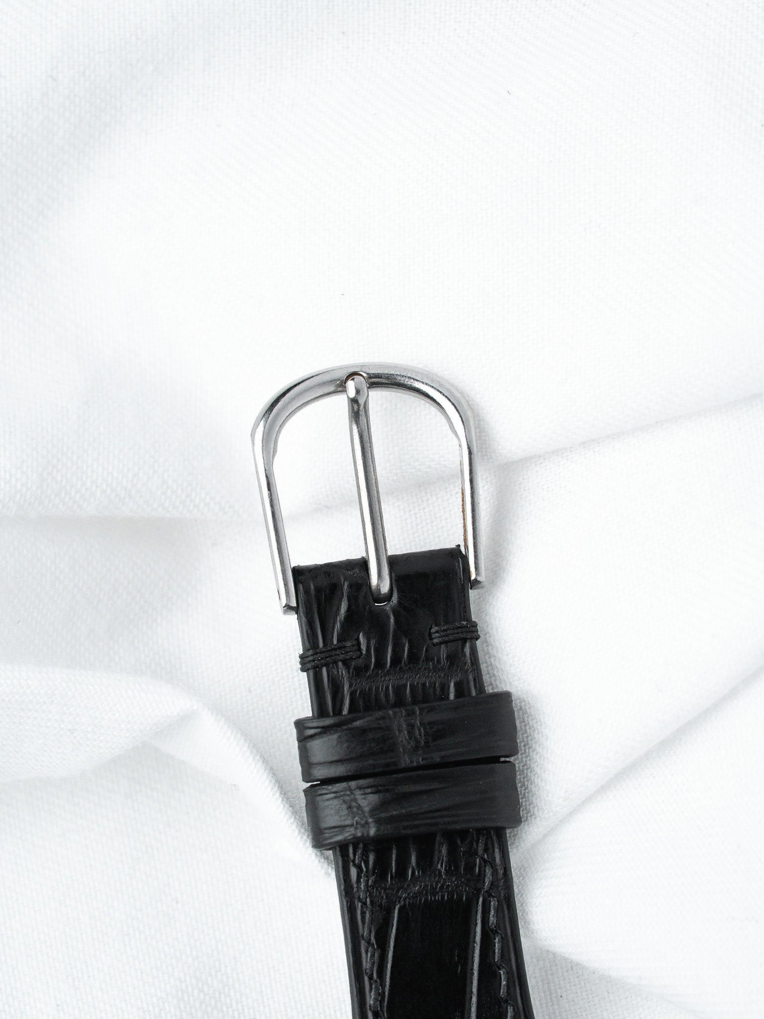 Black alligator leather watch strap with polished steel buckle on white fabric