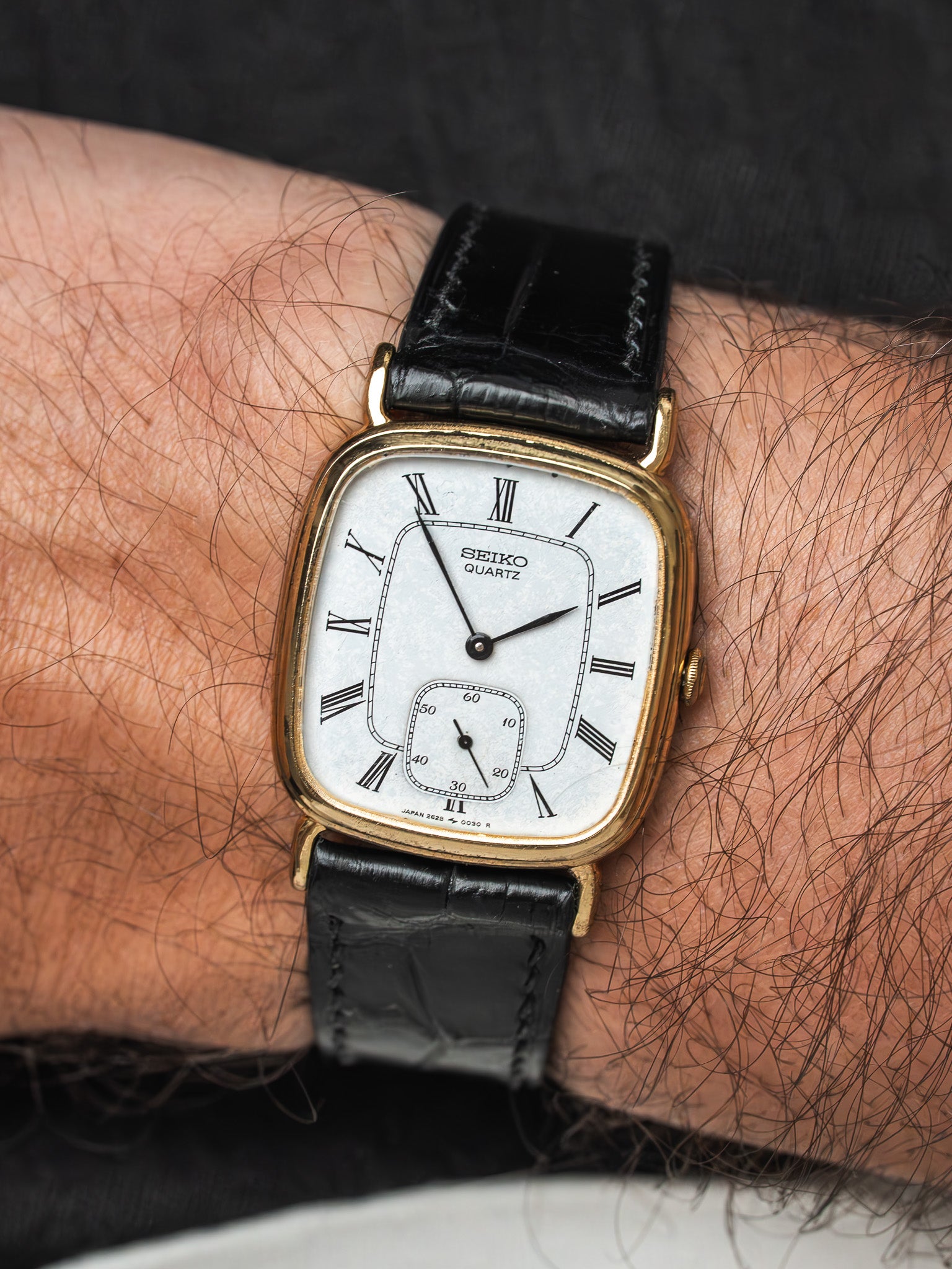 Seiko Quartz vintage watch with gold case, white dial, Roman numerals, black leather strap on wrist