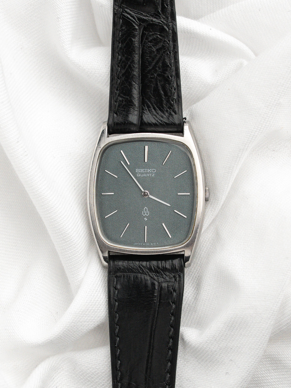 Montre Seiko Quartz vintage avec cadran gris et bracelet en cuir noir texturé.