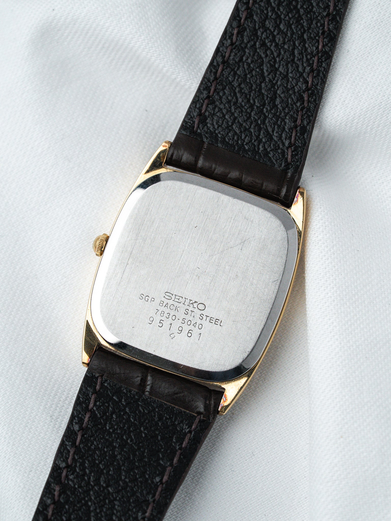 Vintage Seiko watch with gold-tone case, black leather strap, steel back on white fabric