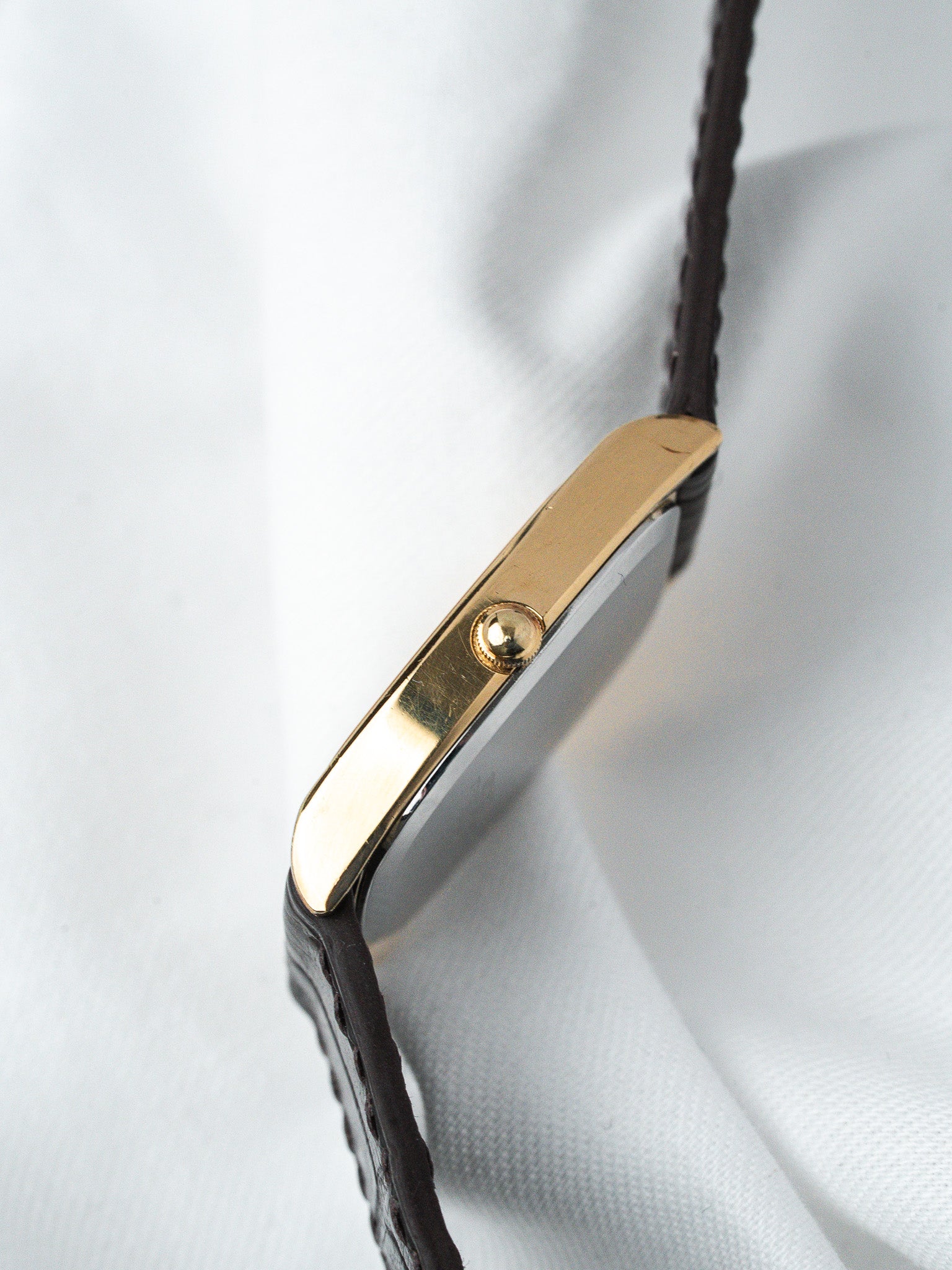 Cartier Tank vintage watch with gold case and brown leather strap on white fabric