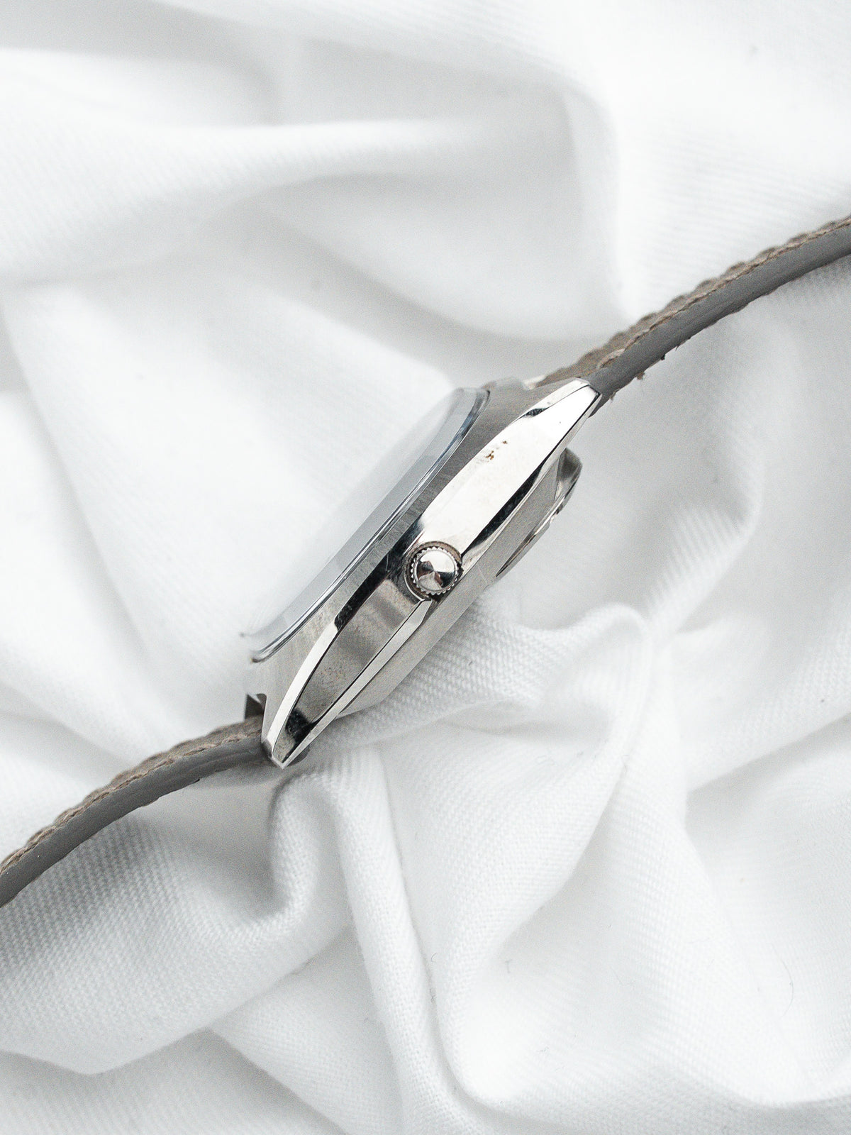 Montre vintage avec boîtier argenté et bracelet en cuir gris sur fond blanc