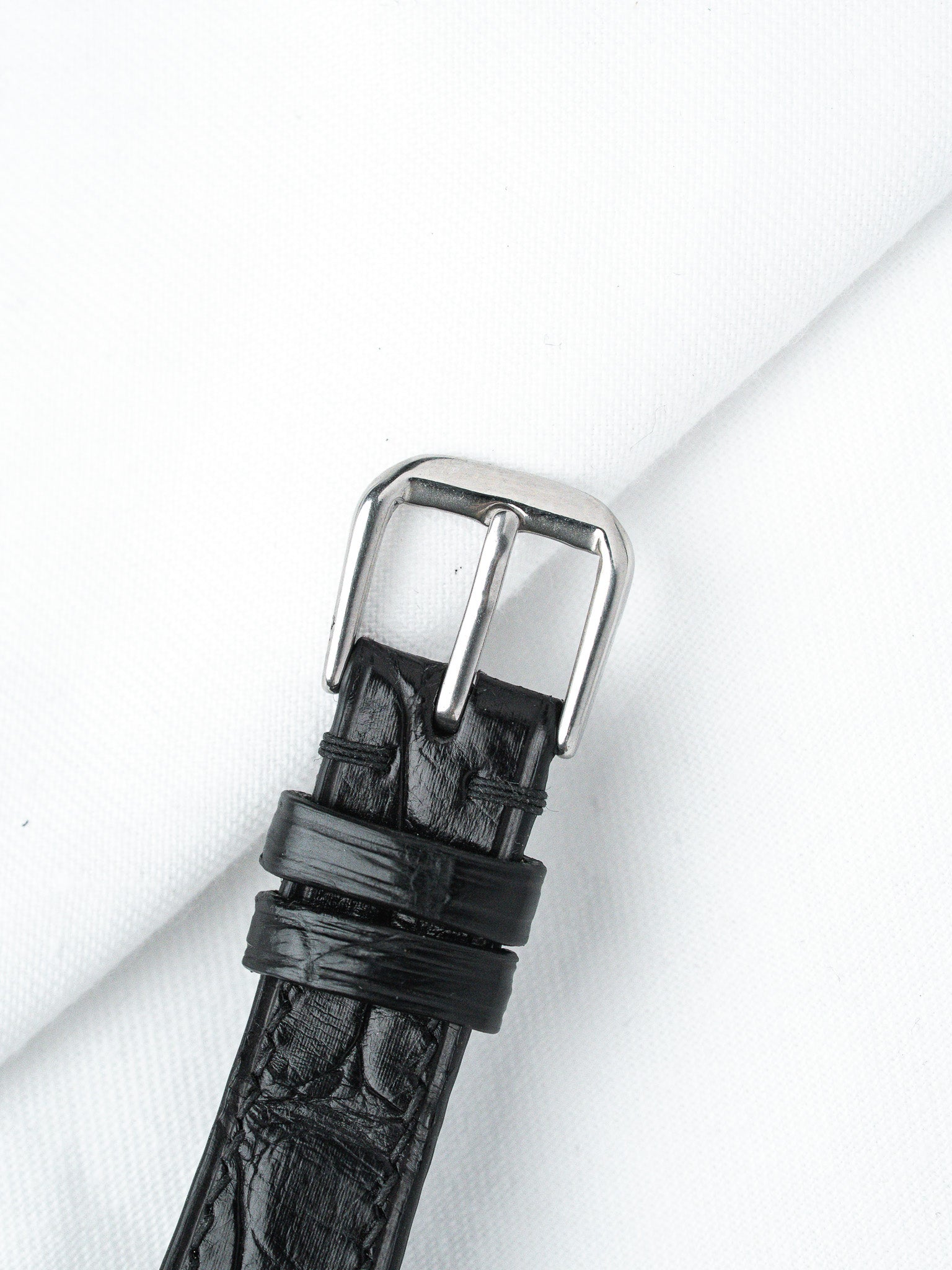 Black alligator leather watch strap with polished steel buckle on white background