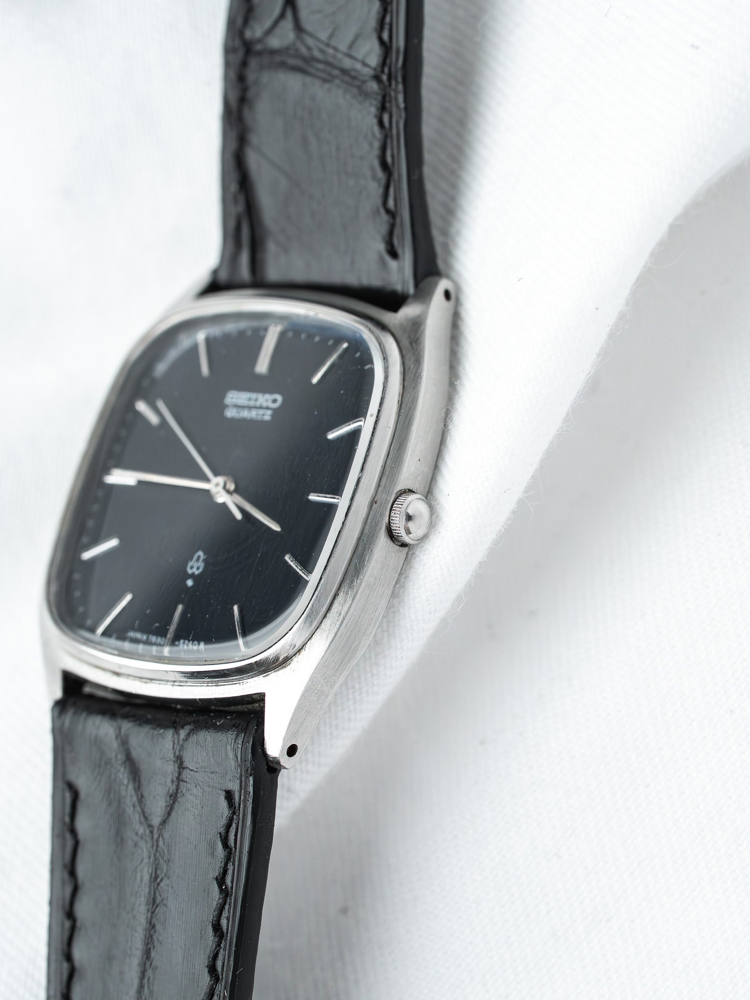 Seiko vintage watch with black dial, silver case, and black leather strap on white background