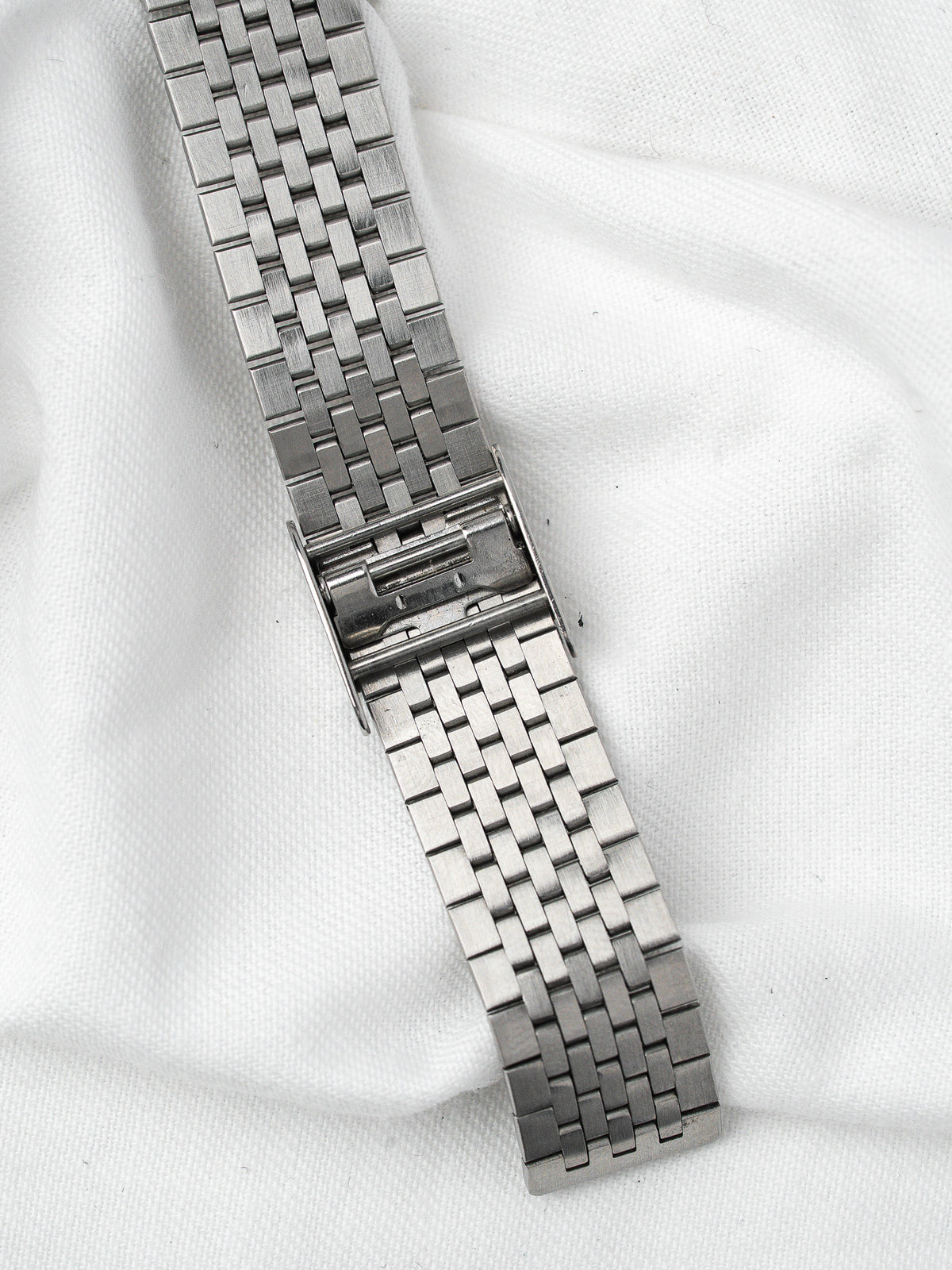 Vintage steel watch bracelet with intricate link design on white fabric