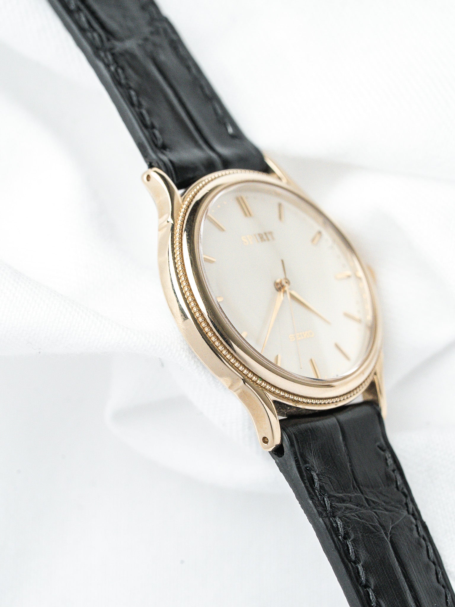 Seiko Spirit vintage watch with gold case, white dial, black leather strap on white background