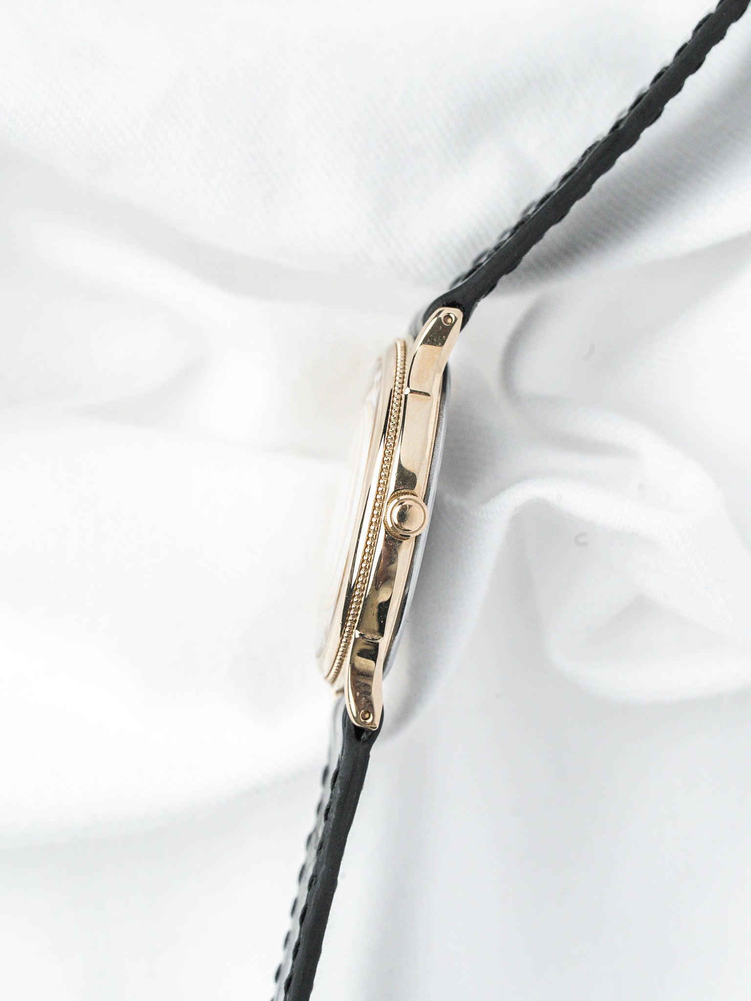 Vintage Cartier watch with gold case, black leather strap, side profile on white fabric
