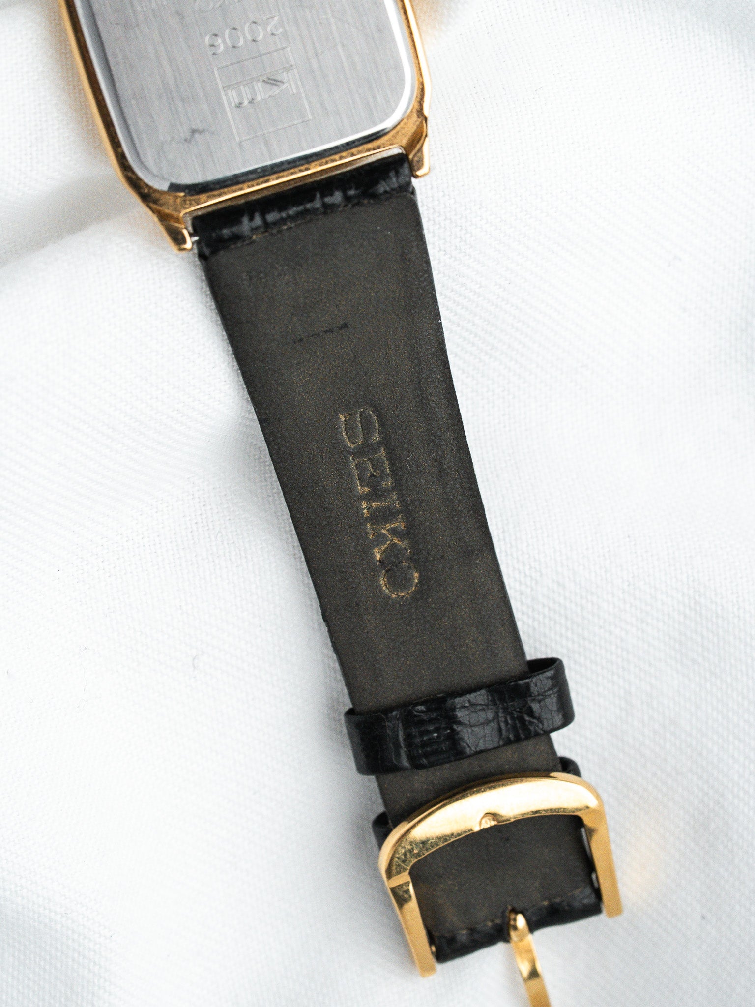 Seiko vintage watch with gold case, black leather strap, and gold buckle on white background