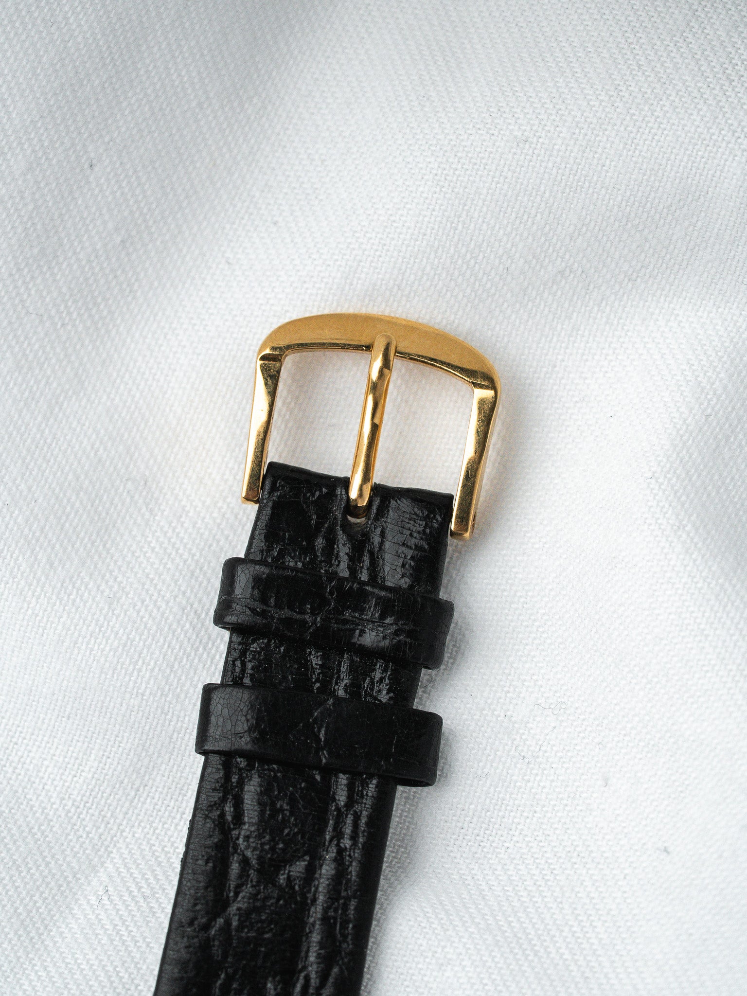 Black alligator leather watch strap with gold buckle on white fabric