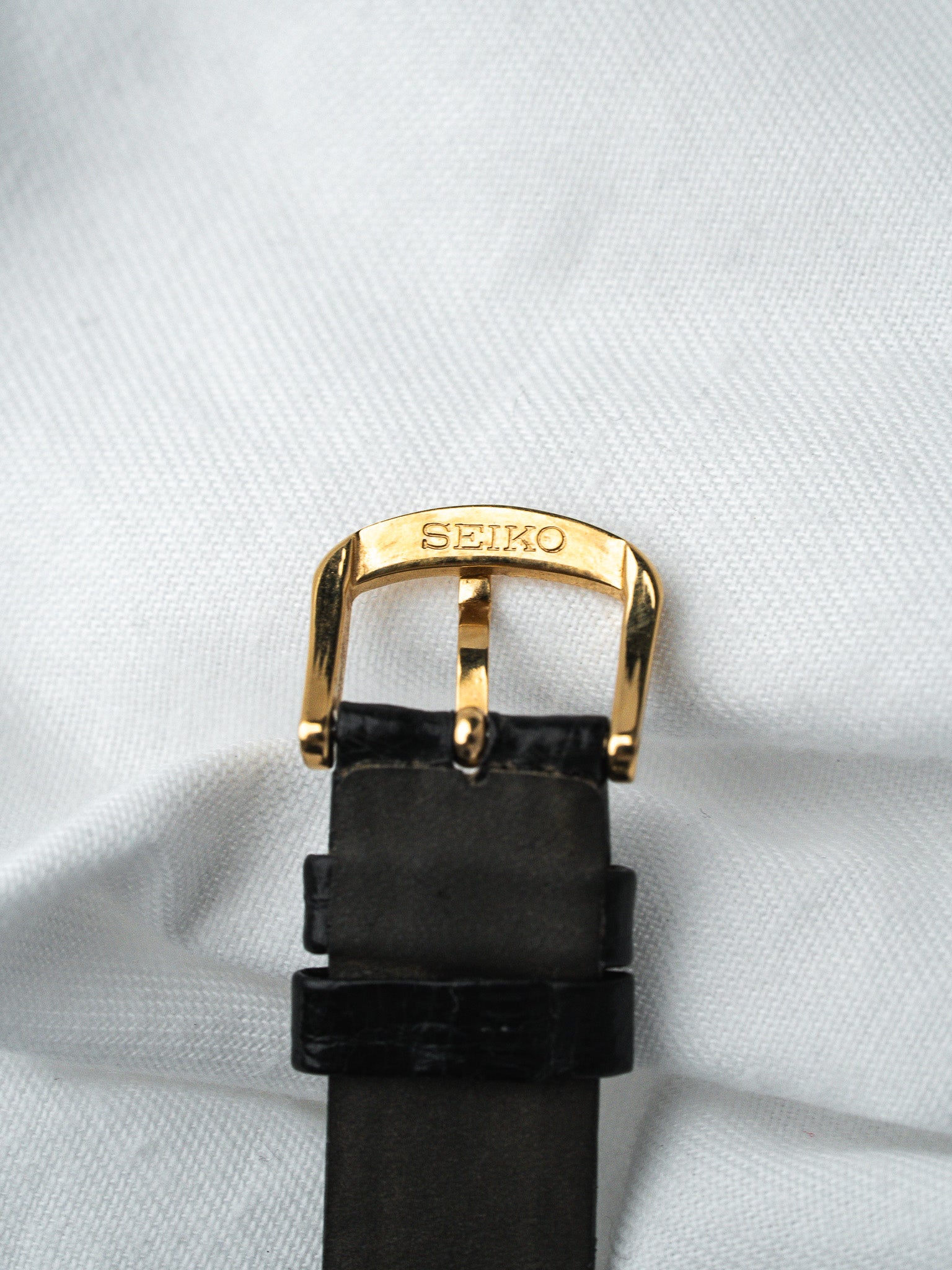Seiko vintage watch with gold buckle and black leather strap on white fabric