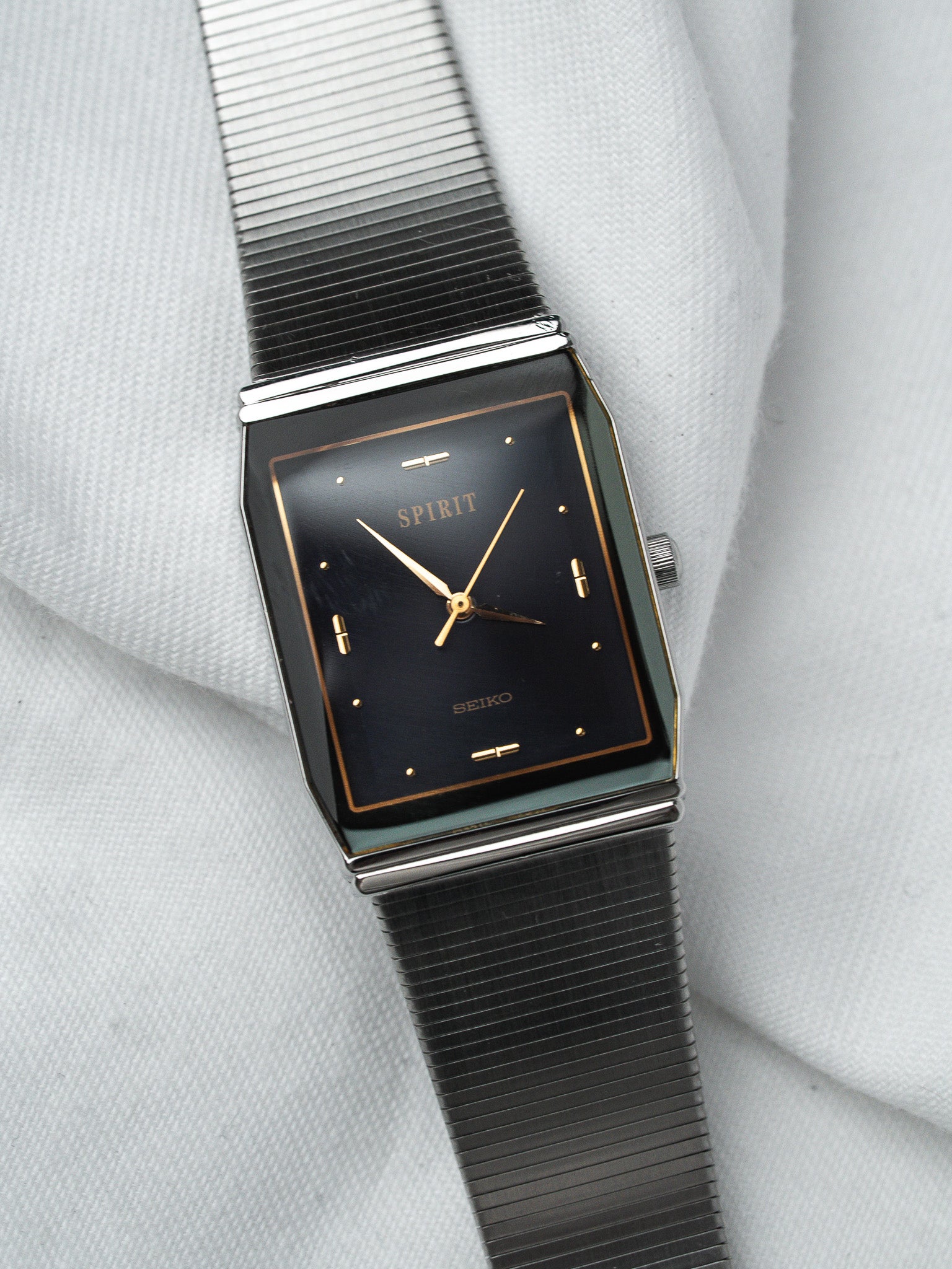 Seiko Spirit vintage watch with black dial, gold hands, and mesh bracelet on white fabric