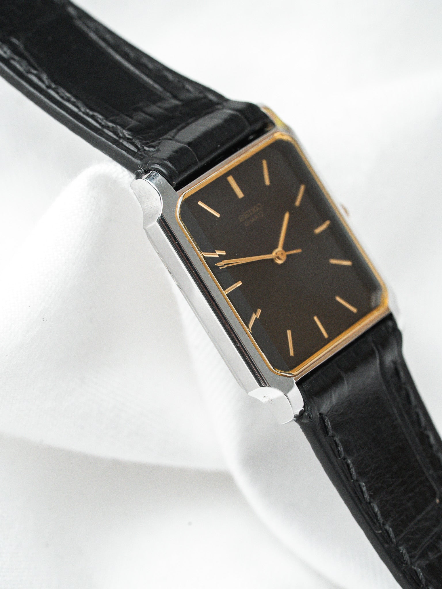Seiko vintage watch with black dial, gold markers, and black leather strap on white display
