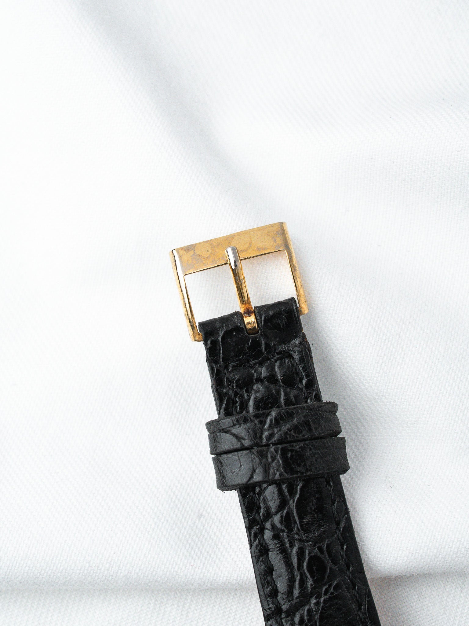 Black alligator leather watch strap with gold buckle on white fabric