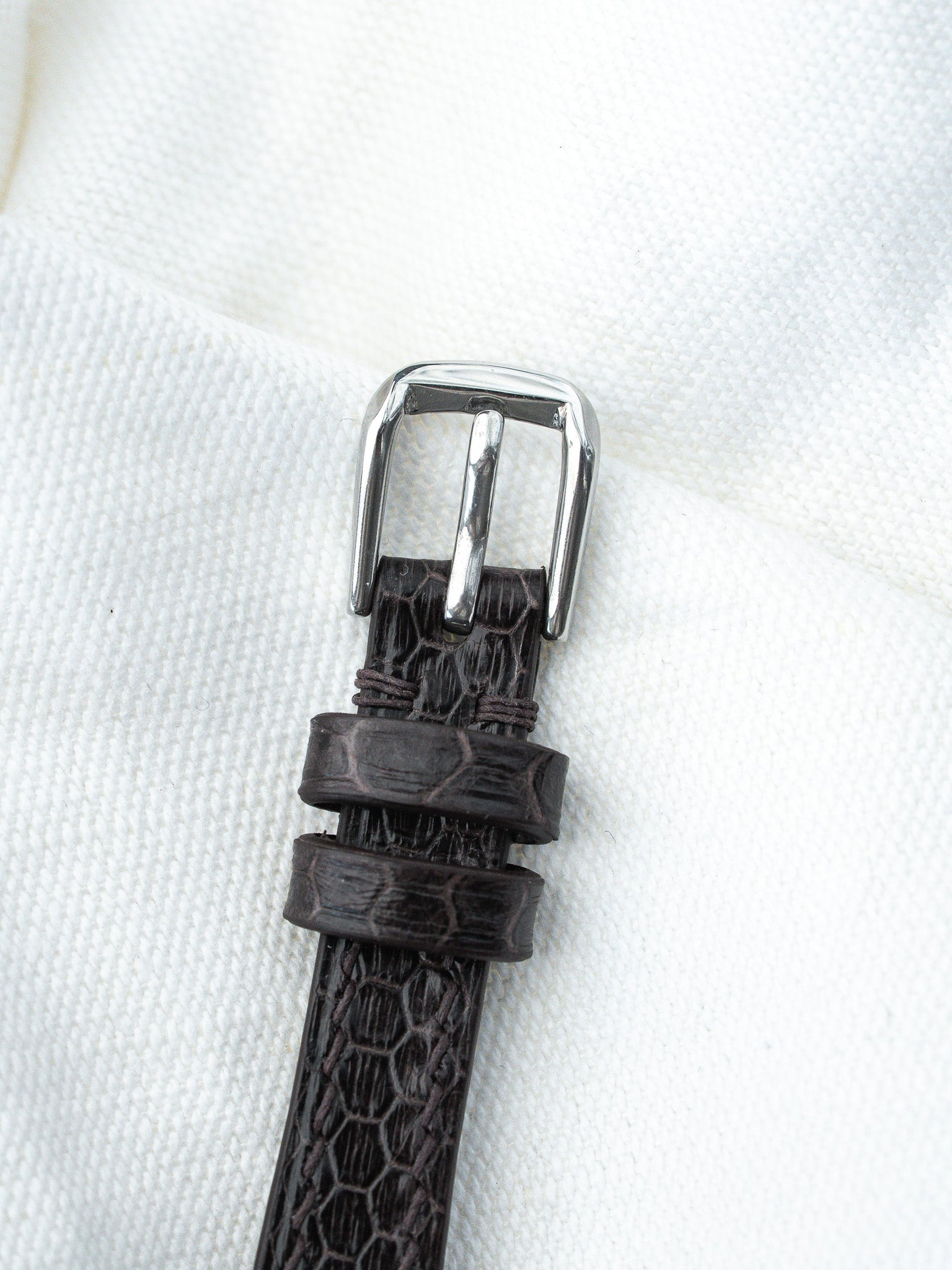Dark brown alligator leather watch strap with polished steel buckle on white fabric