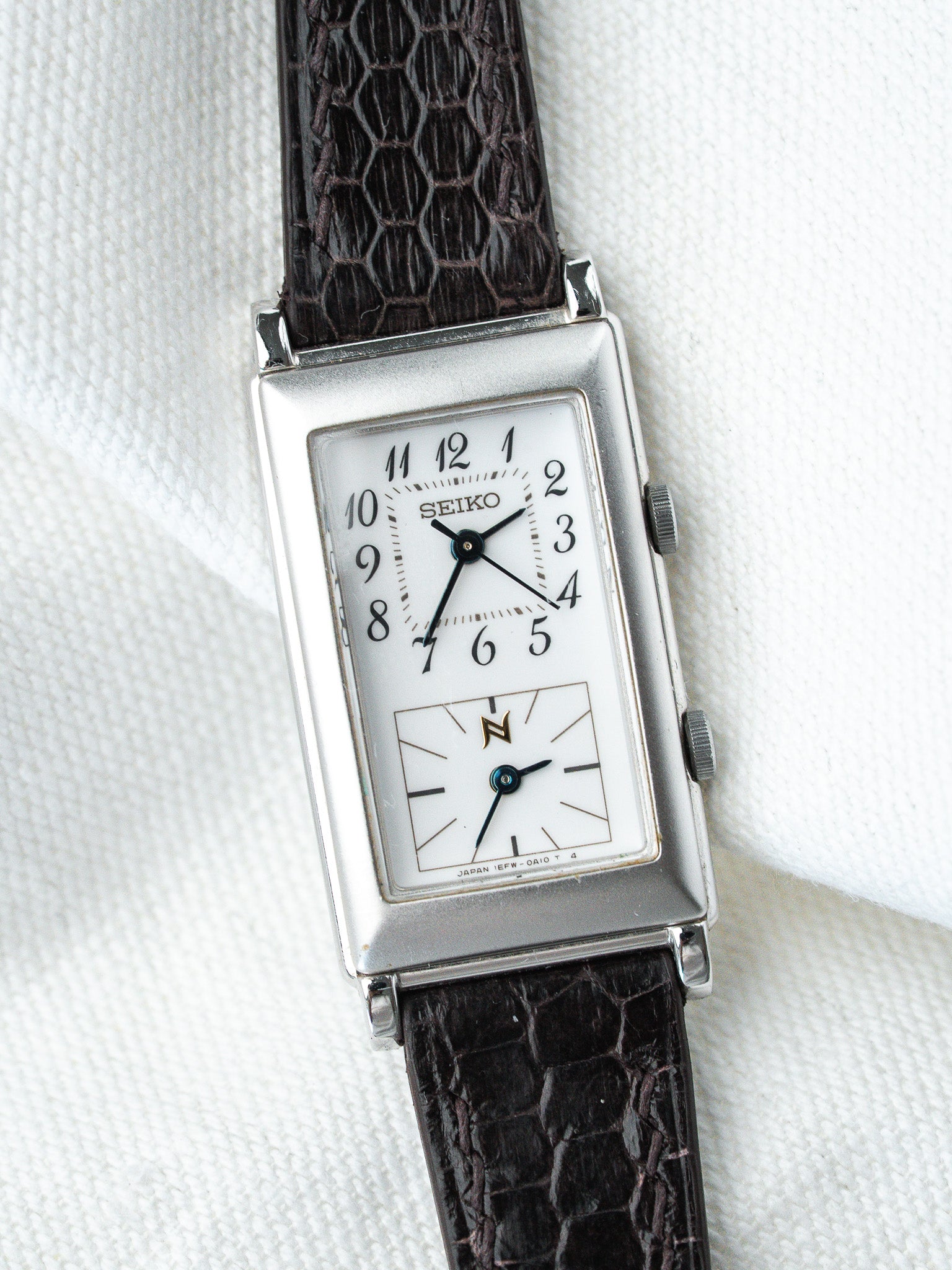 Vintage Seiko rectangular watch with white dial, black crocodile strap, on textured white background