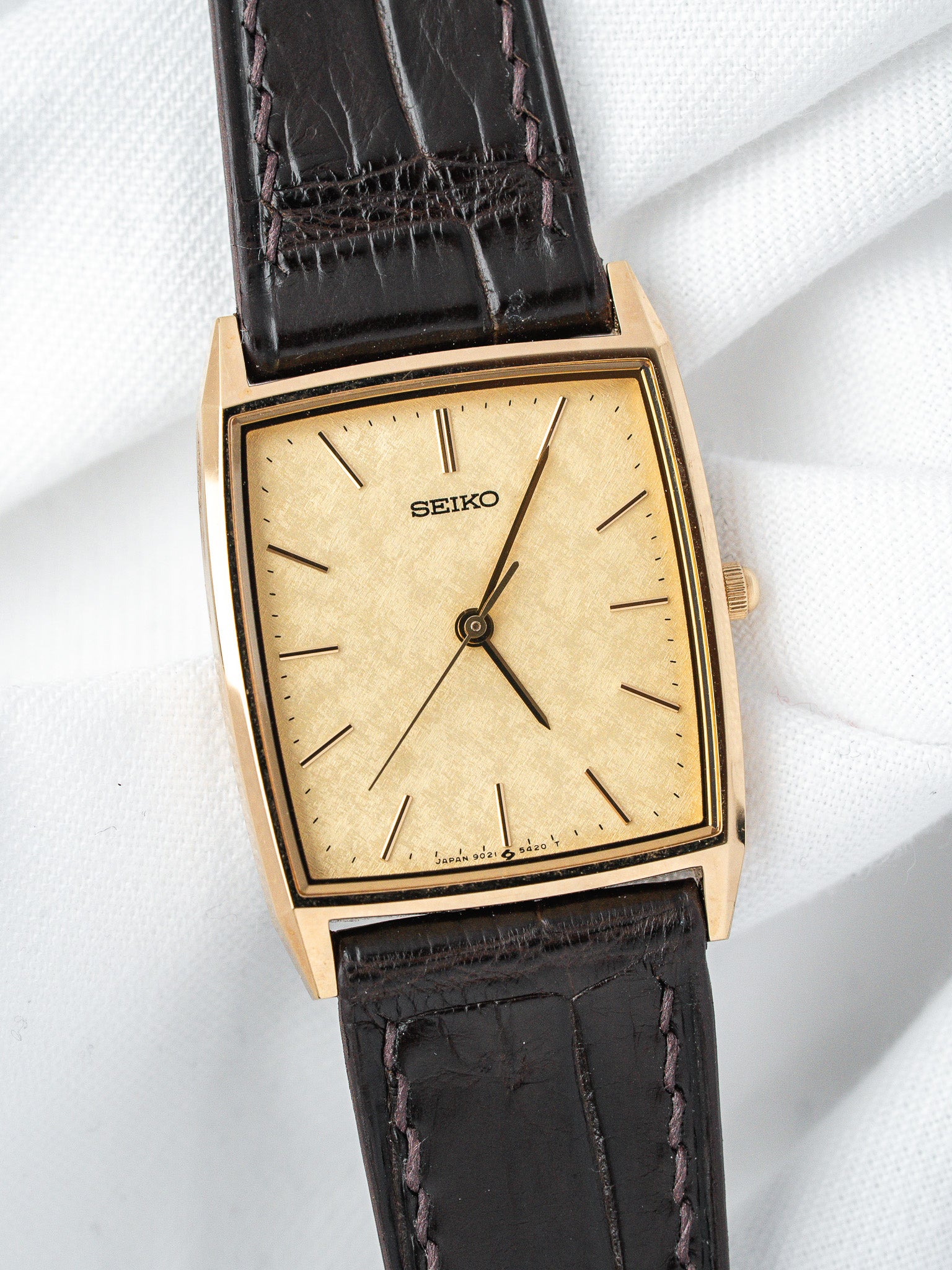 Seiko vintage watch with gold-tone case, cream dial, black leather strap on white background