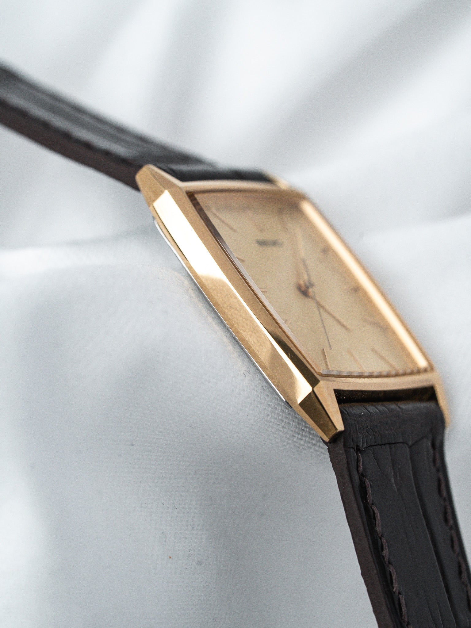 Vintage Universal Genève tonneau watch with gold case, cream dial, black leather strap on white fabric