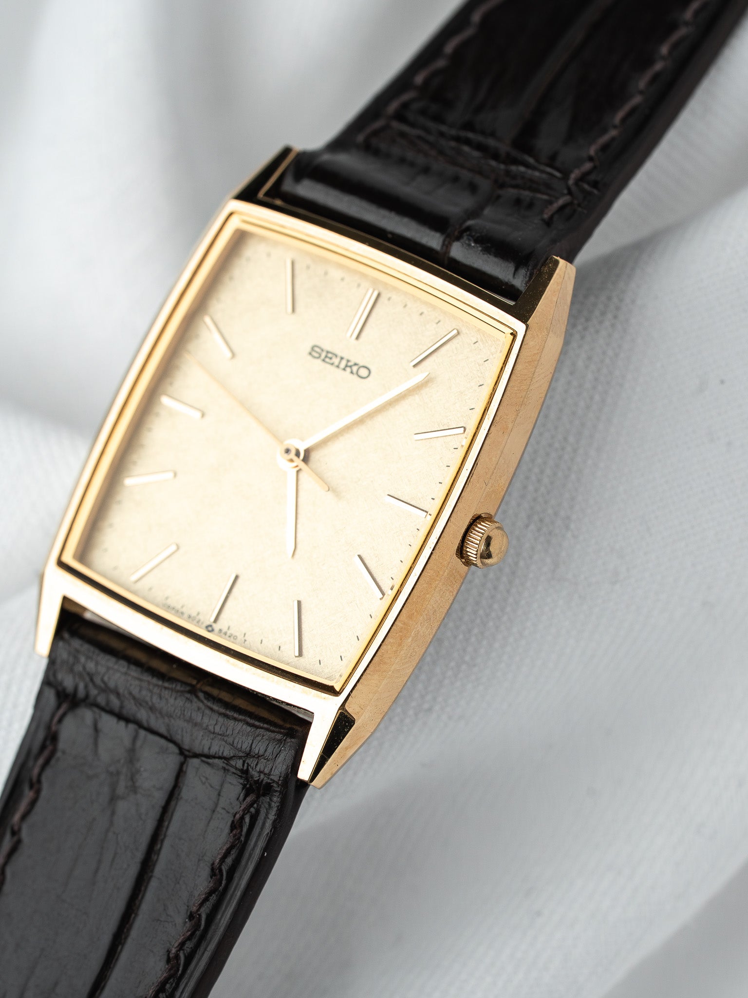 Seiko vintage watch with gold case, cream dial, black leather strap on white background